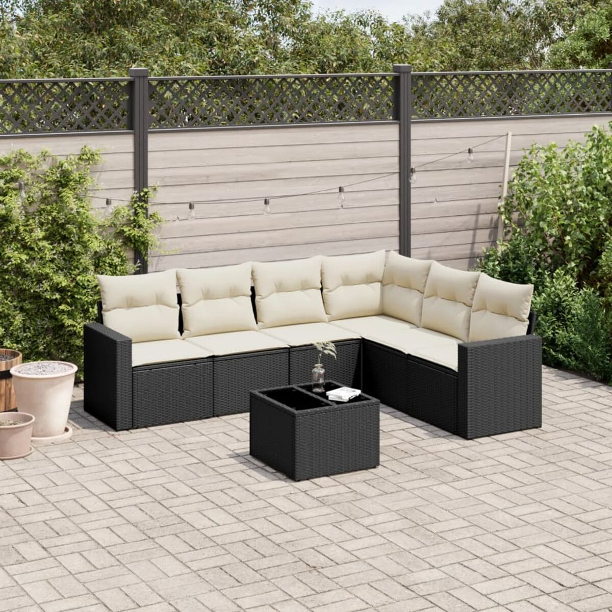 Un divano componibile nero da esterno con cuscini color crema è su un patio in mattoni. Un tavolo quadrato nero è al centro.
