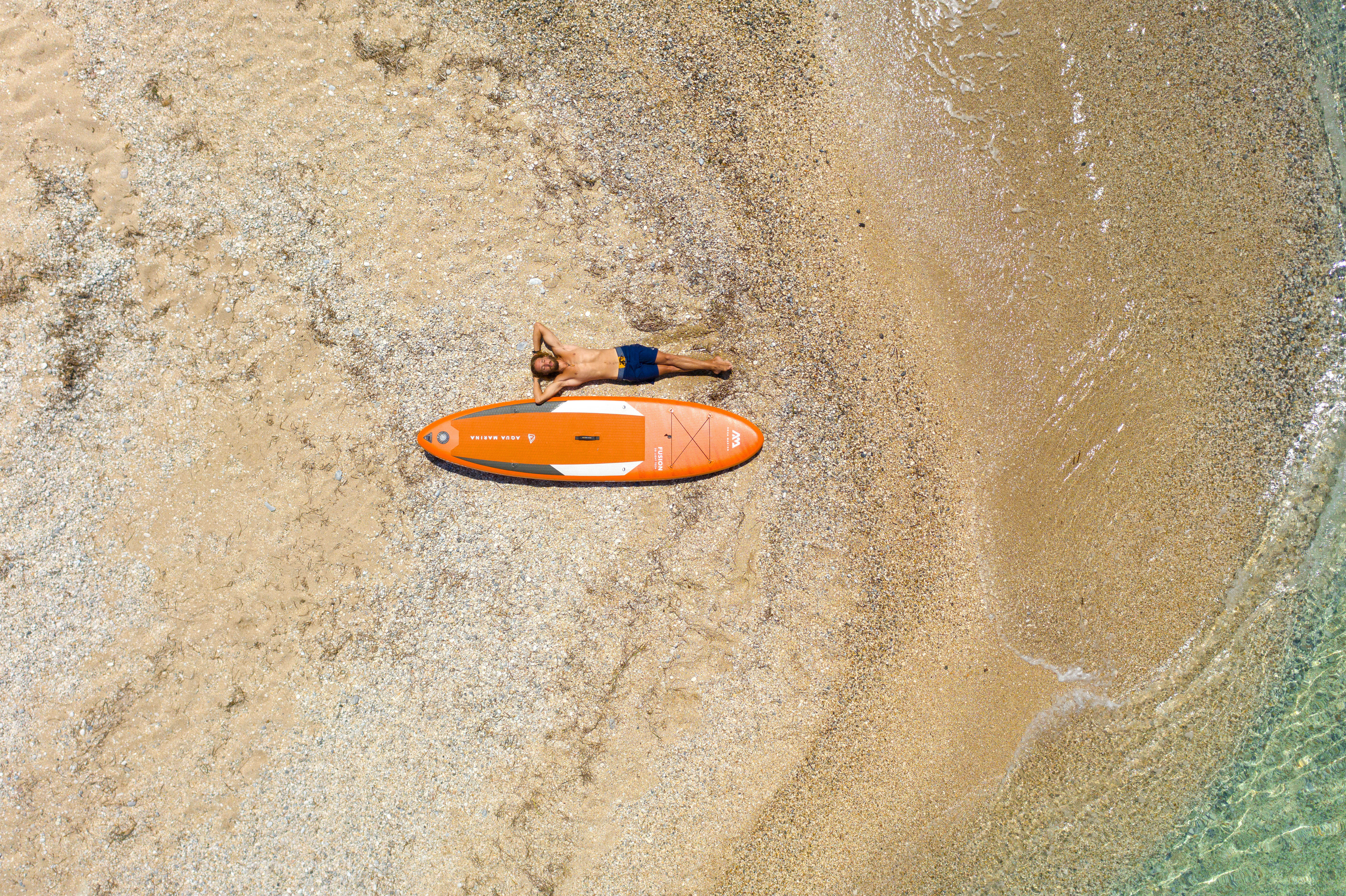 Draufsicht einer Person auf einem Paddleboard in klarem Wasser in der Nähe eines Sandstrandes.
