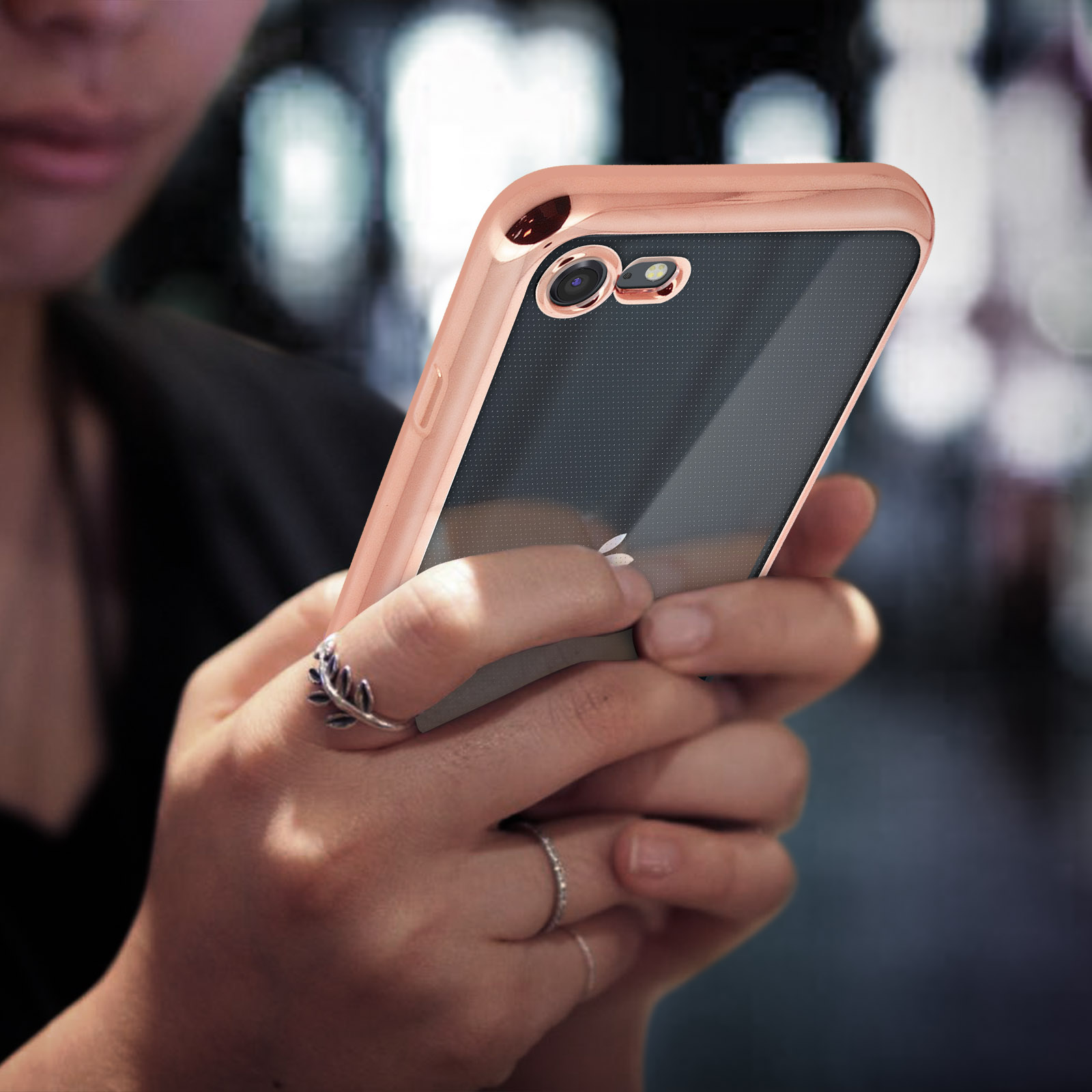 Una donna che tiene un telefono in una custodia oro rosa. Anello d'argento al dito.