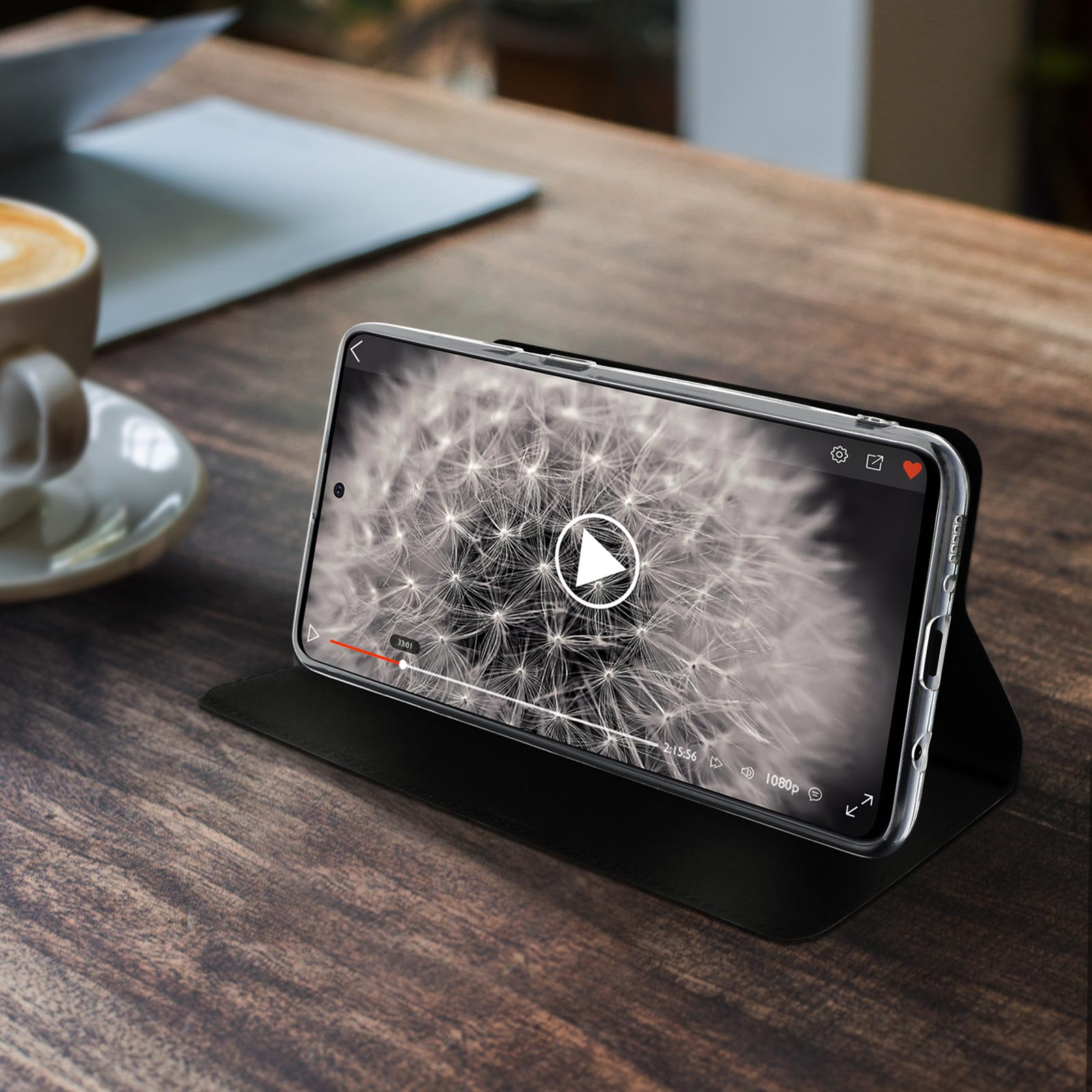 Telefono in una custodia su un tavolo di legno che riproduce un video. Tazza di caffè a sinistra.