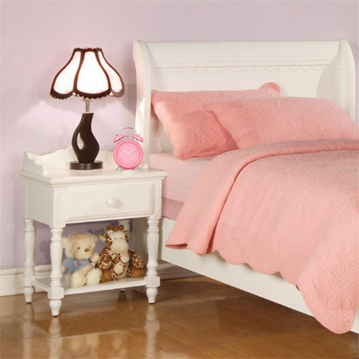 Schlafzimmer. Weißer Nachttisch mit Lampe, Wecker und Stofftieren. Rosa Bett und Wand.