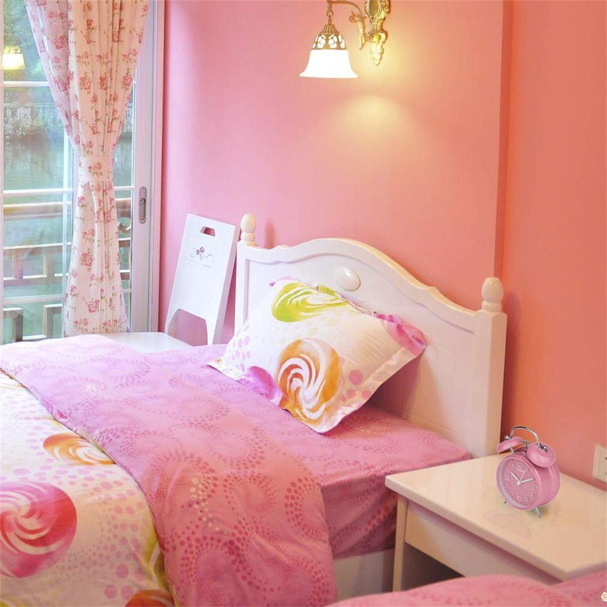 Rosa Schlafzimmer mit Bett, floralen Vorhängen und Nachttisch mit Wecker.