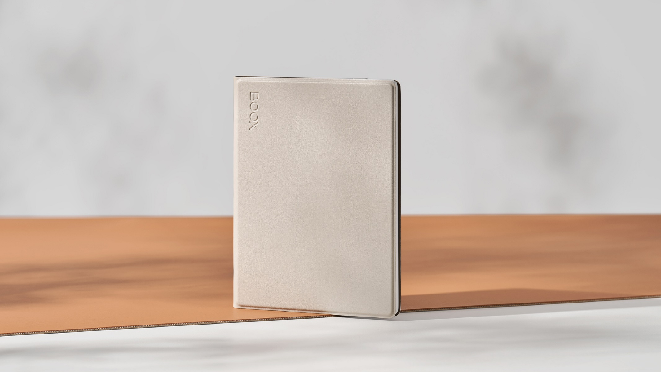 E-reader color crema con copertina marrone chiaro. 'BOOX' è scritto sul dispositivo. Sfondo neutro.