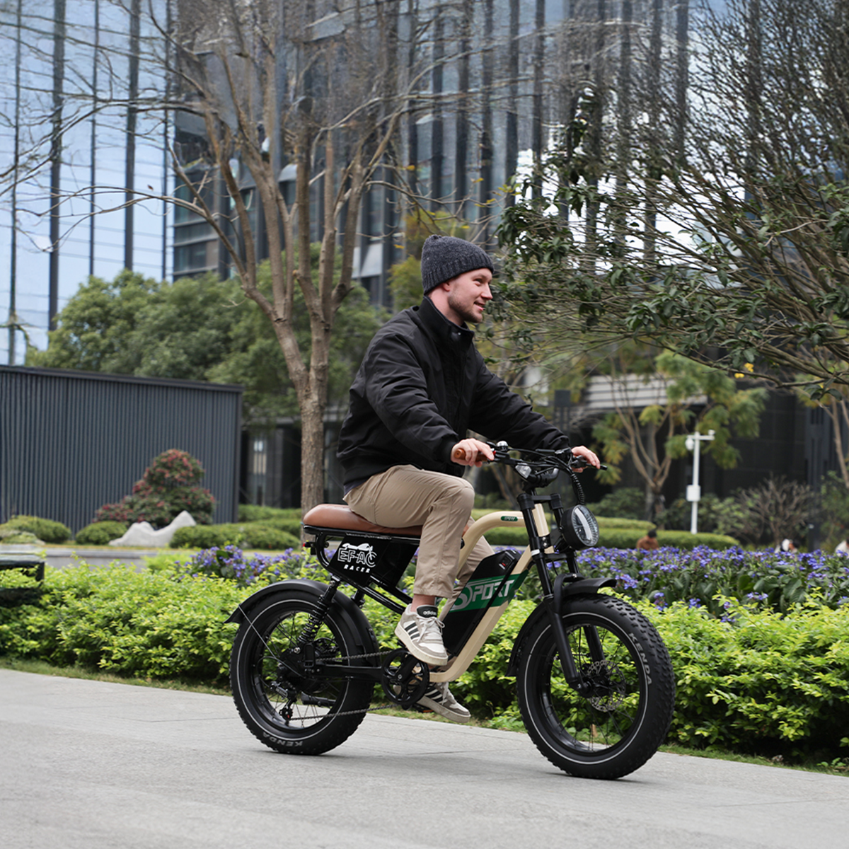 Mężczyzna jadący na czarnym rowerze po drodze. Zielone krzewy i drzewa po bokach. Słoneczny dzień.