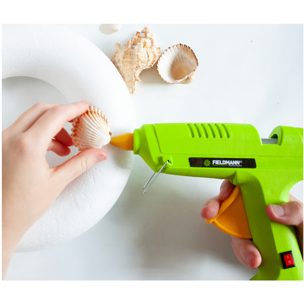 Una persona incolla una conchiglia su un anello di schiuma bianco con una pistola per colla verde.
