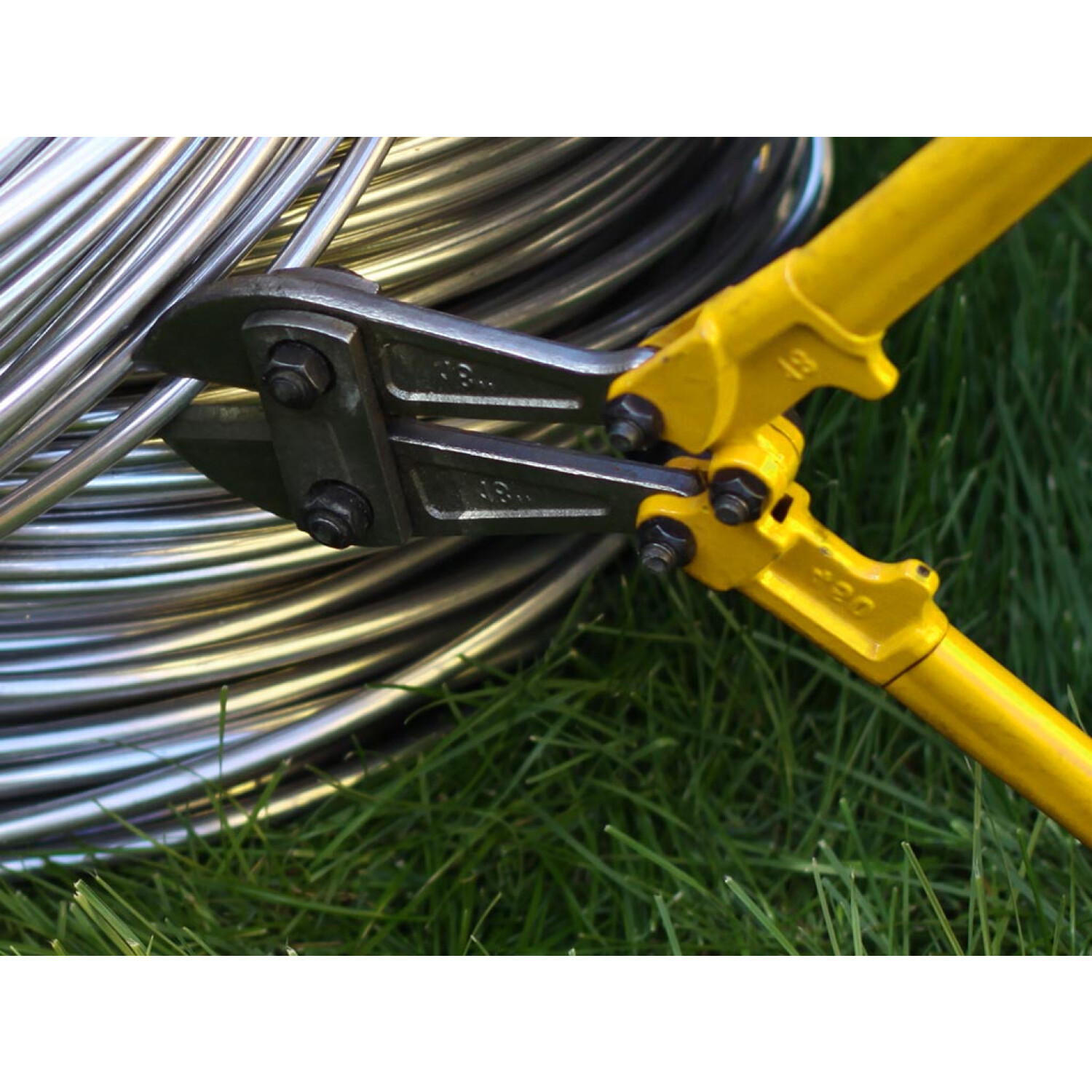 Ein gelber Bolzenschneider auf grünem Gras, mit einer Spule aus silbernen Metallstangen.