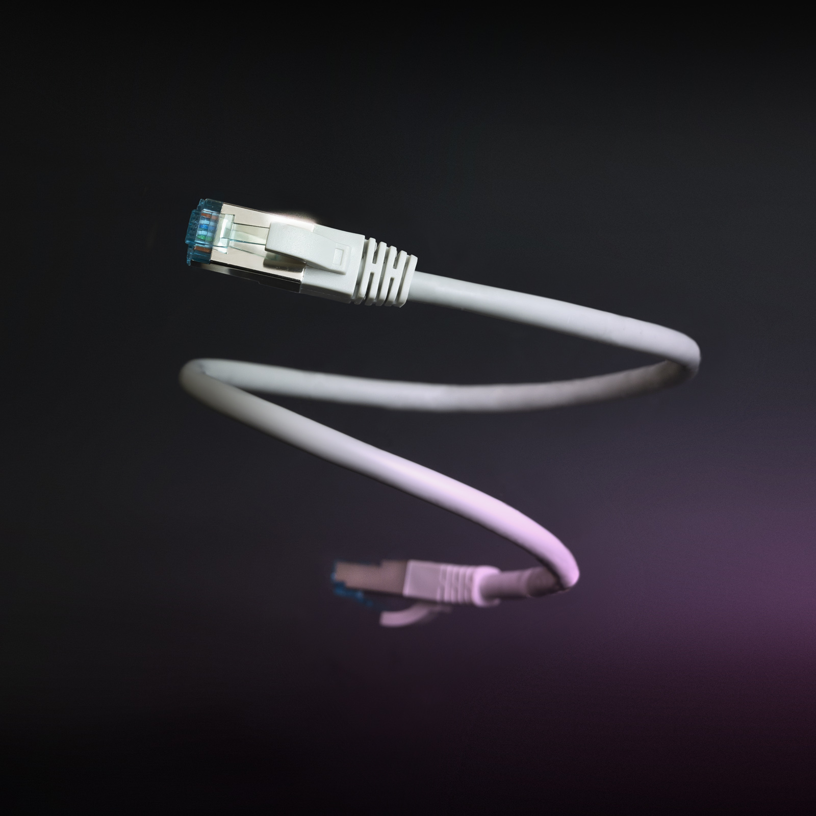 Witte netwerkkabel met blauwe connectoren, spiraalvormig tegen een donkere achtergrond. Licht reflecteert op de kabel.
