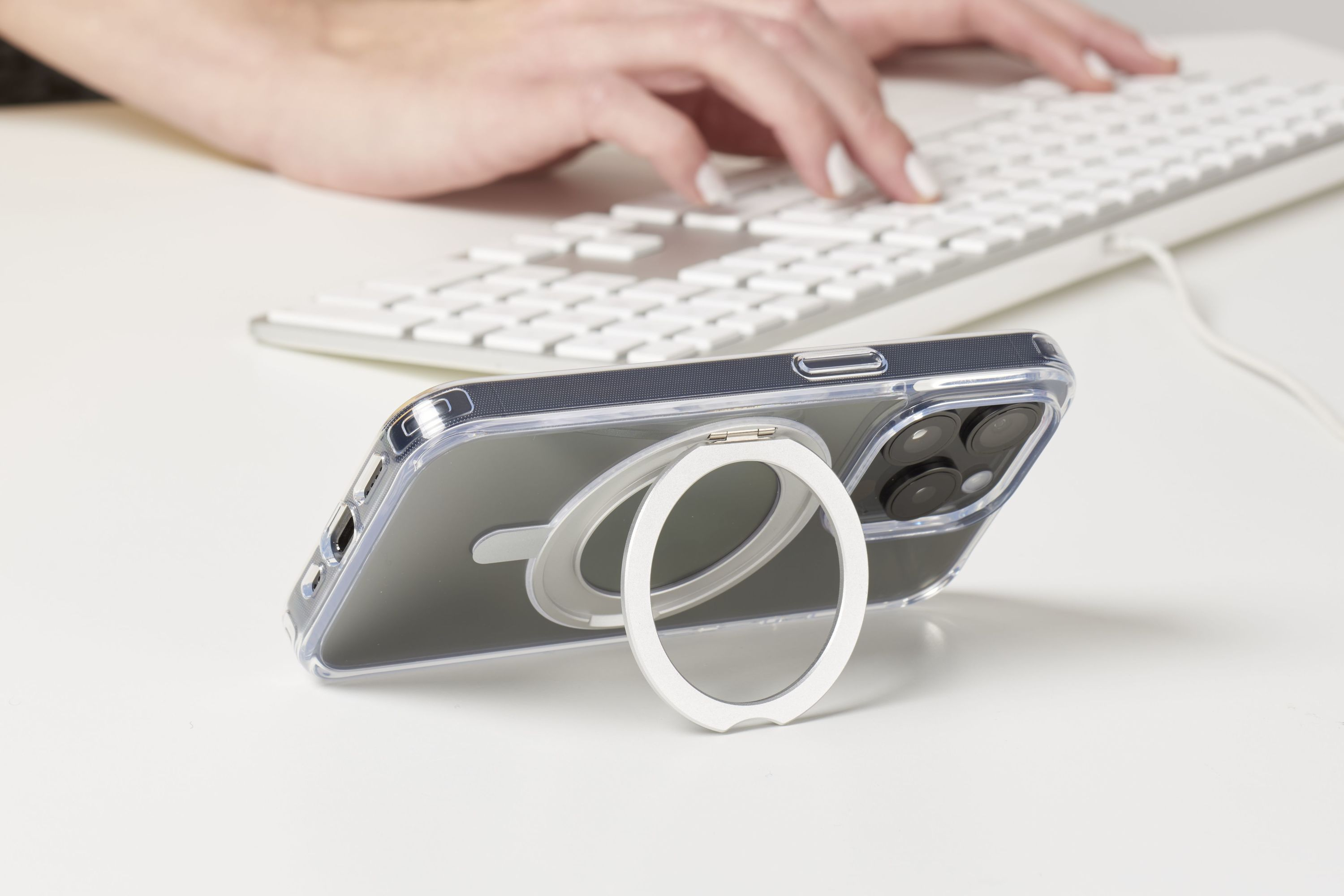 Téléphone avec support anneau sur bureau blanc, mains tapant sur clavier.