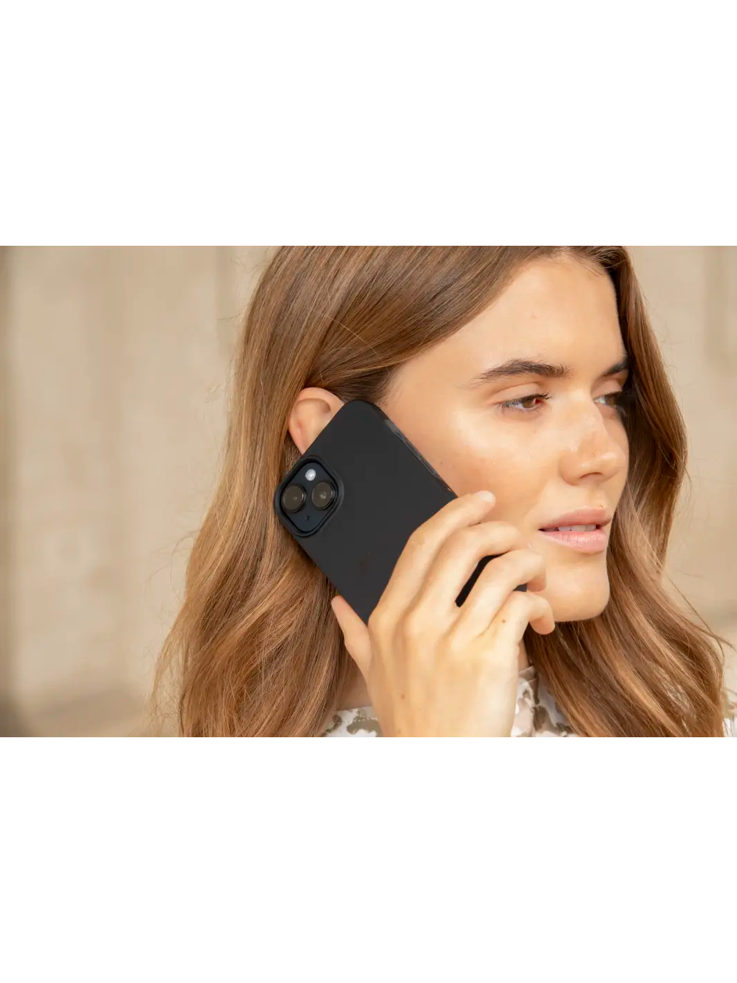 Una donna tiene un telefono nero vicino all'orecchio, guardando il telefono.