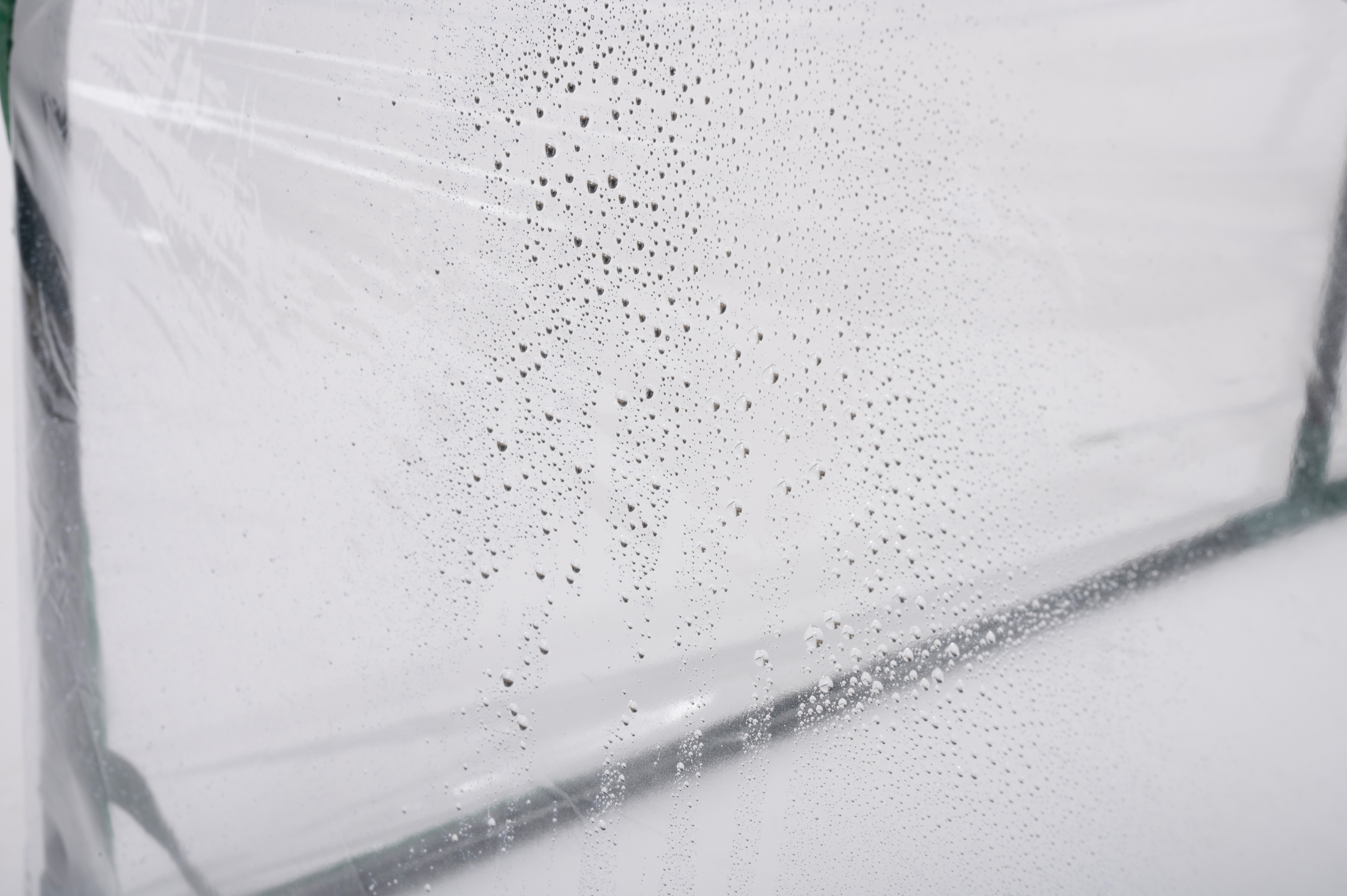 Een doorzichtig plastic vel met waterdruppels erop, tegen een witte achtergrond.