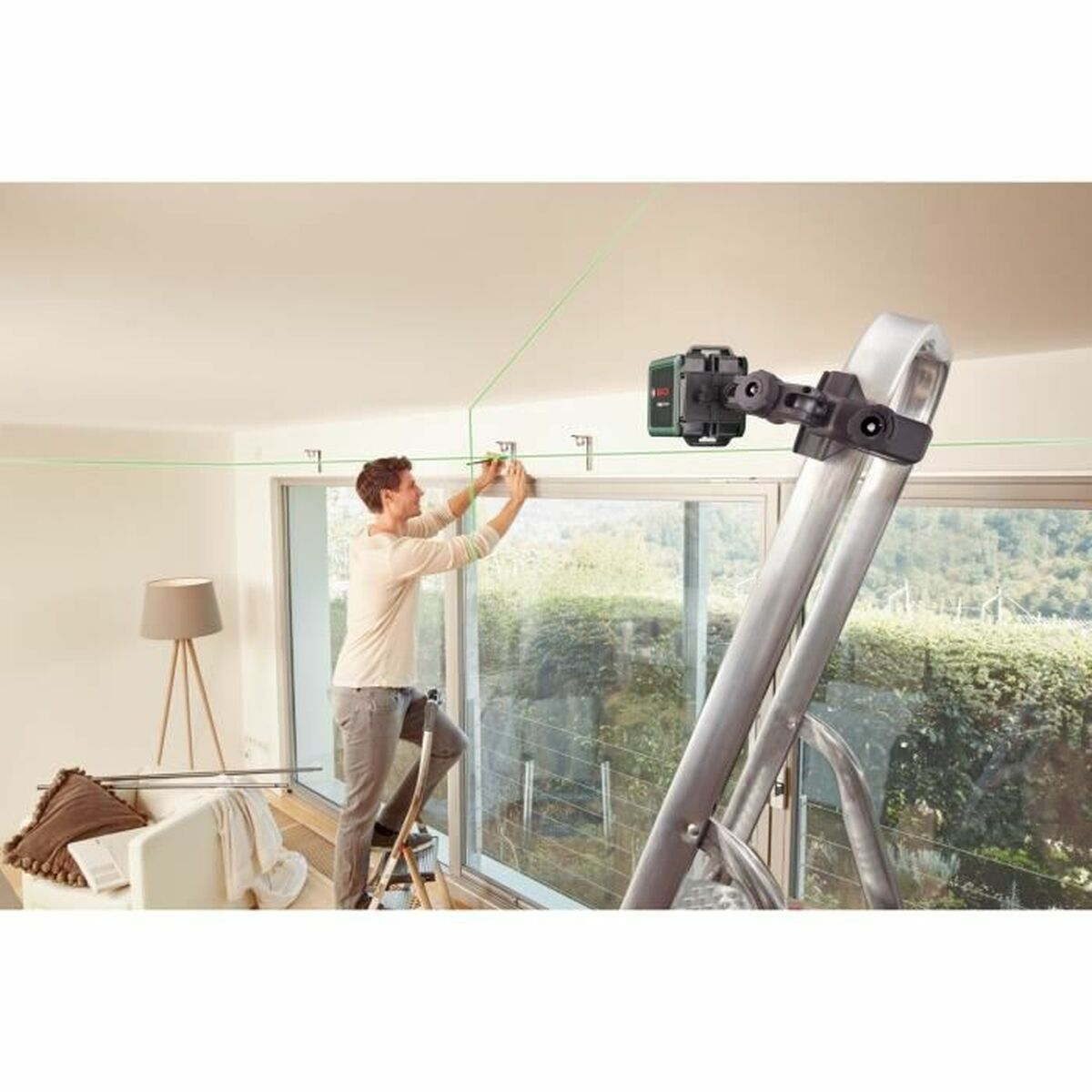 Mężczyzna na drabinie używa poziomicy laserowej. Zielone linie lasera są widoczne na suficie.