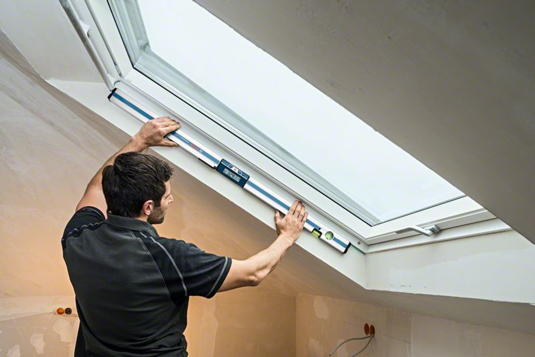 Mężczyzna używa poziomicy do sprawdzenia ramy okna w białym pomieszczeniu.