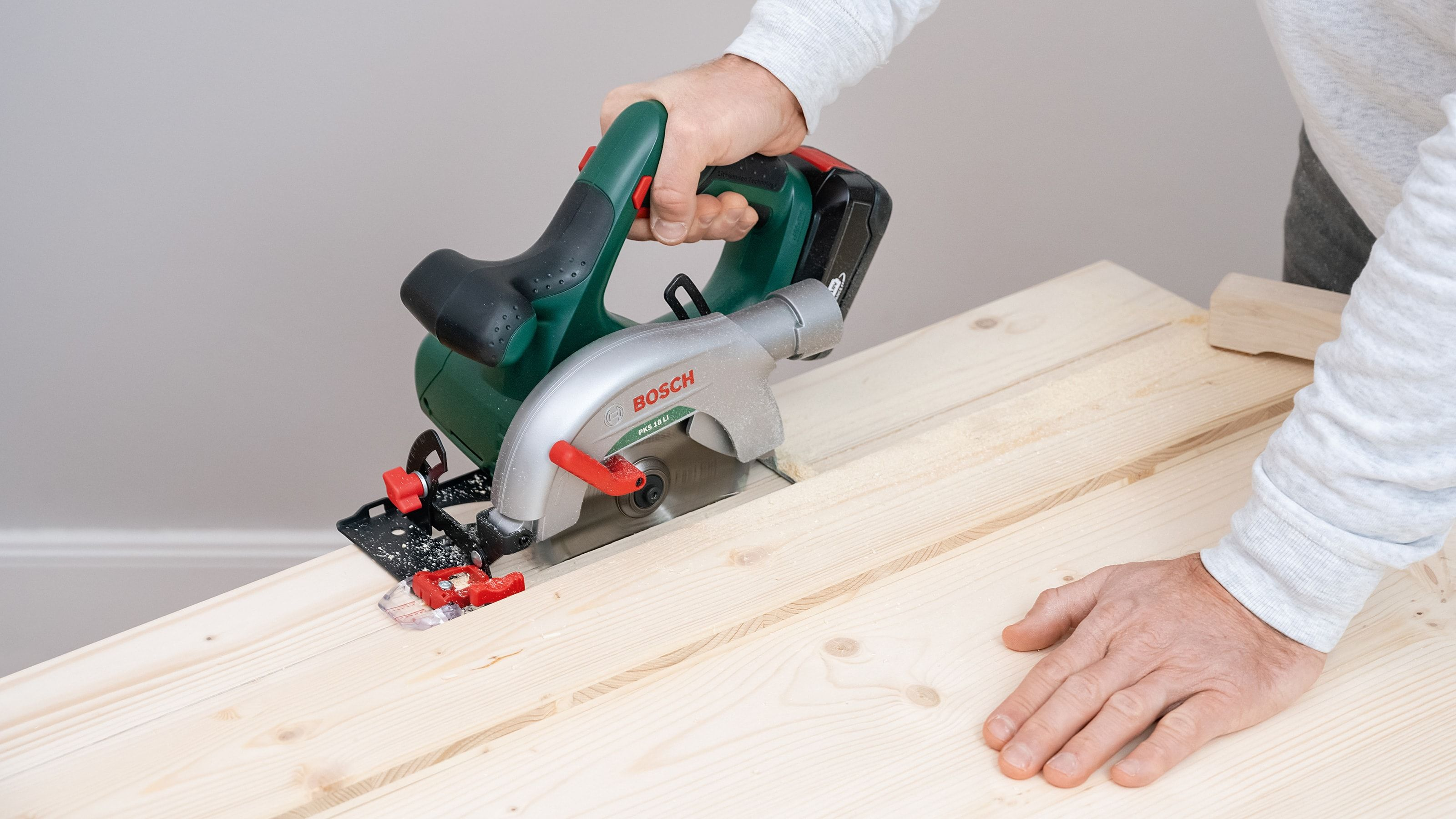 Osoba używająca piły tarczowej do cięcia drewnianej deski. Piła jest zielona i srebrna.