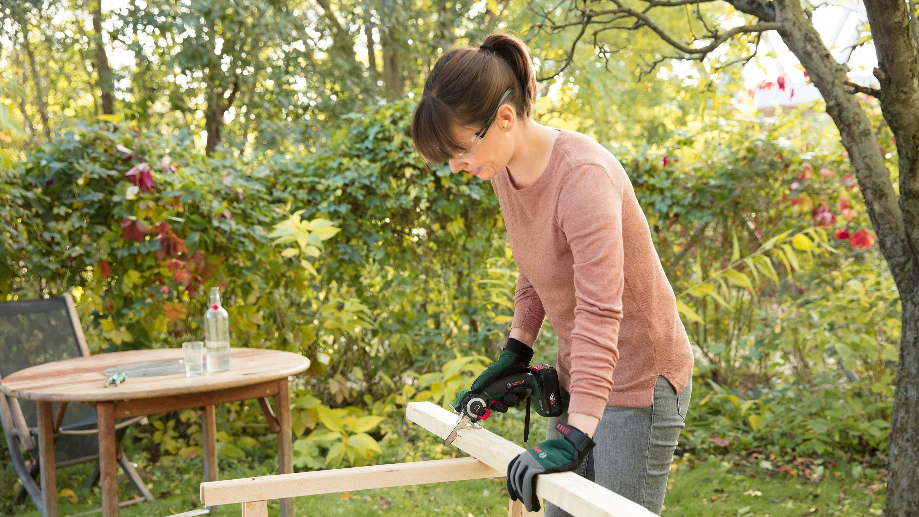 Frau schneidet Holz mit einer Säge in einem Garten.