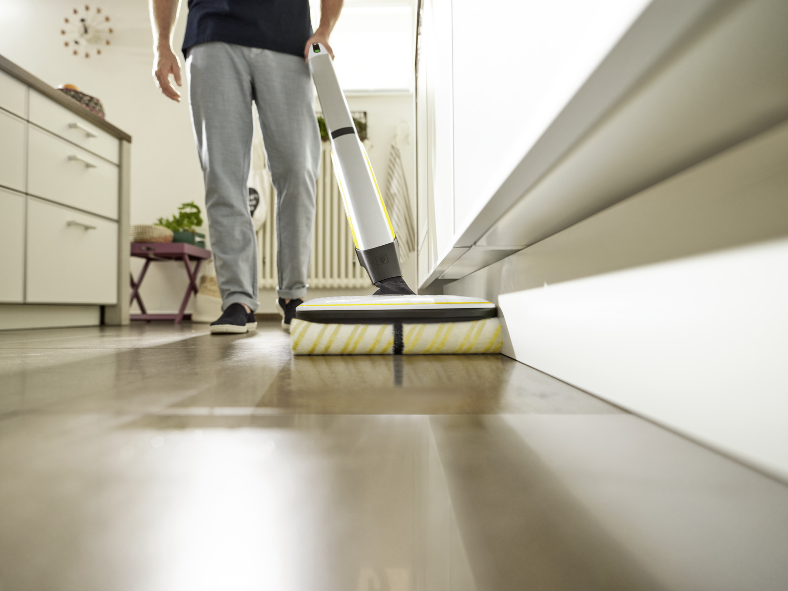 Mężczyzna czyszczący drewnianą podłogę żółto-białą maszyną do czyszczenia podłóg.