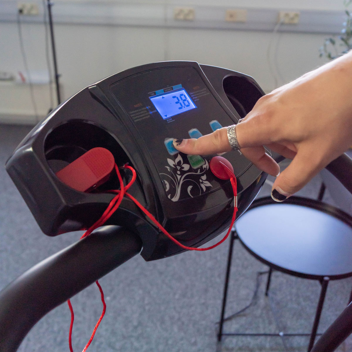 Ręka osoby naciska przycisk na panelu sterowania bieżni.