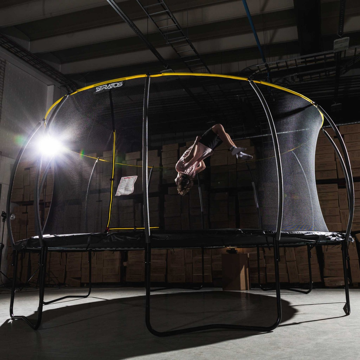 Eine Person macht einen Rückwärtssalto auf einem Trampolin. Das Trampolin ist von einem Sicherheitsnetz umgeben.