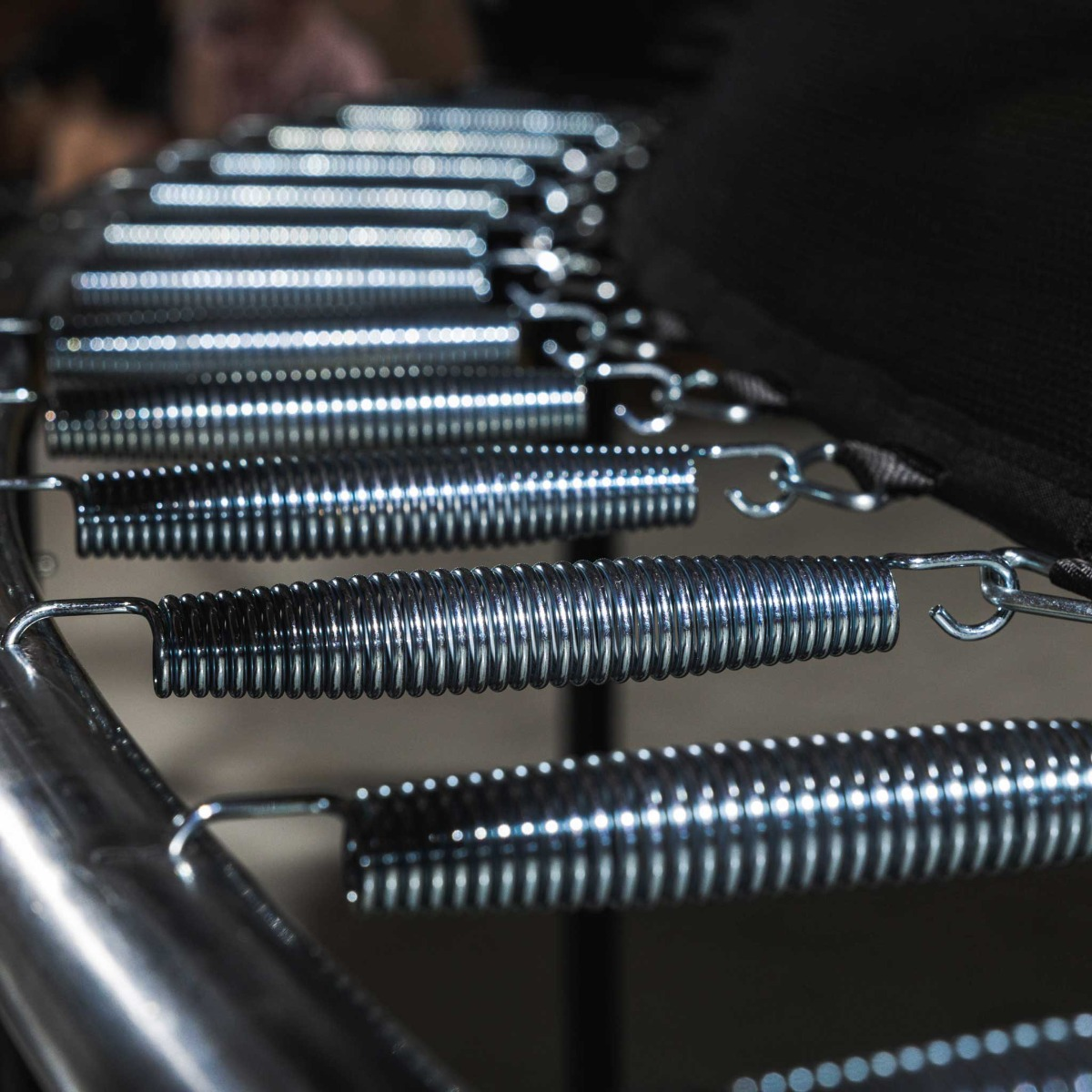 Nahaufnahme von Metallfedern an einem Trampolinrahmen. Die Federn sind silberfarben.