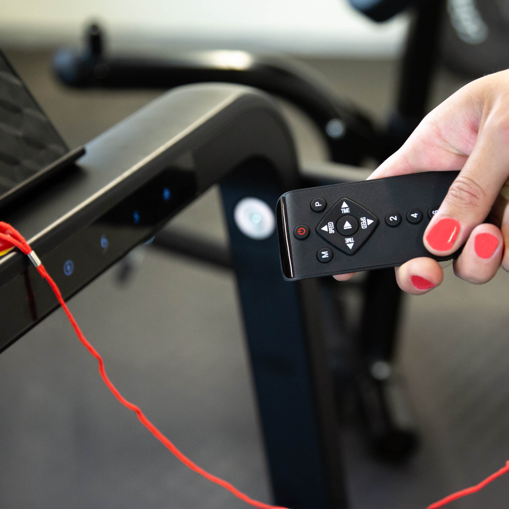 Ręka trzymająca pilota nad urządzeniem do ćwiczeń.