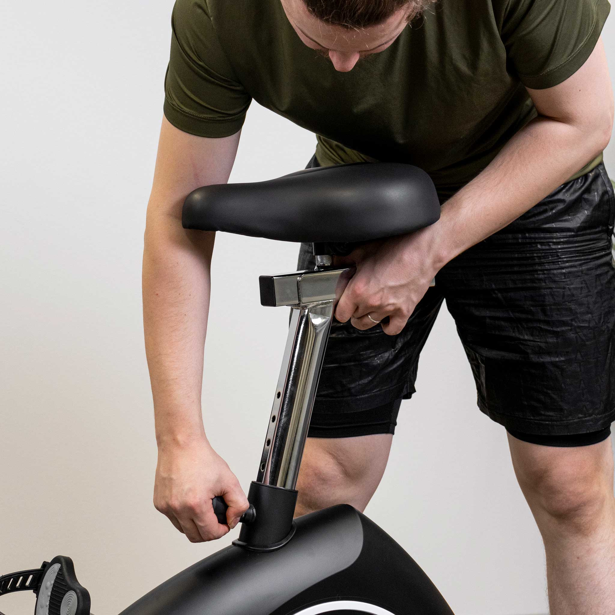 Osoba reguluje siodełko roweru stacjonarnego. Rower jest czarny i srebrny.