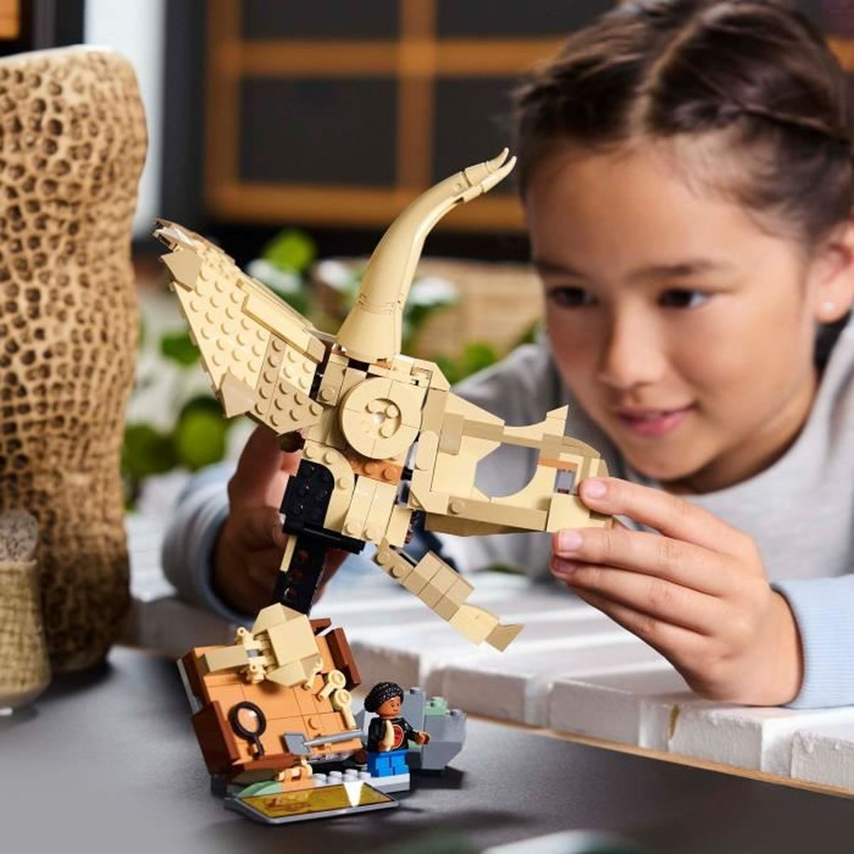 Una niña juega con una cabeza de dinosaurio Lego. Hay una pequeña escena Lego delante.