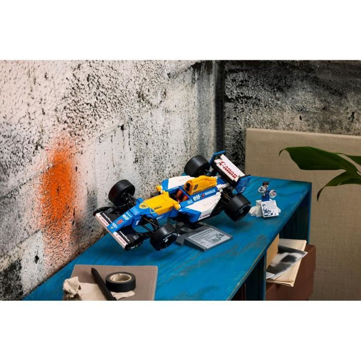 Samochód wyścigowy LEGO na niebieskim stole, z tłem graffiti i skrzynką narzędziową.