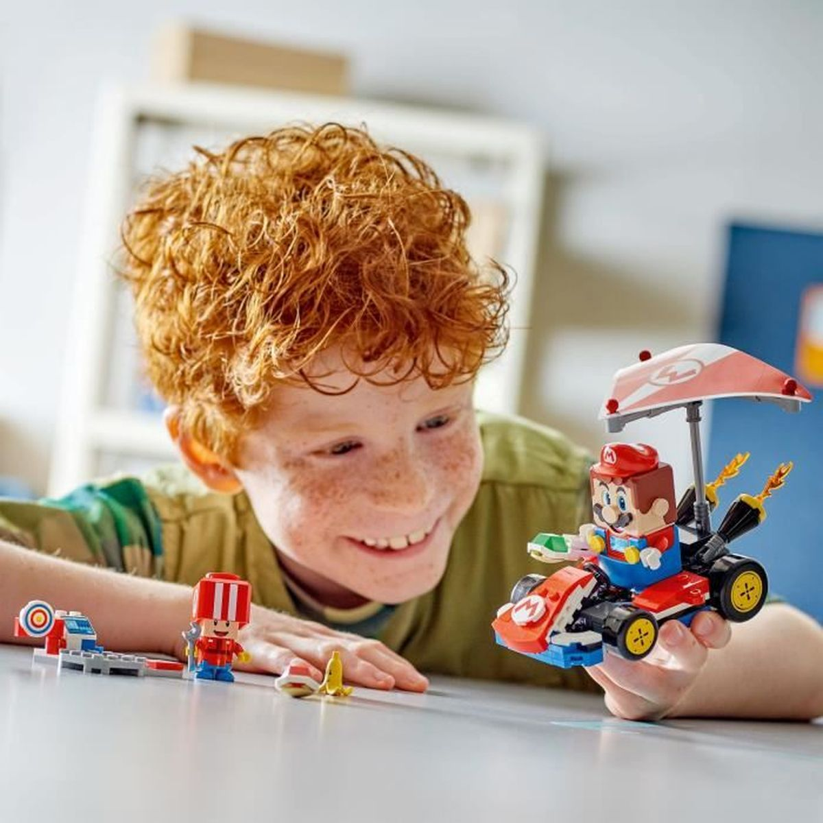 Un garçon sourit en regardant un kart Lego Mario. D'autres pièces Lego sont sur la table.