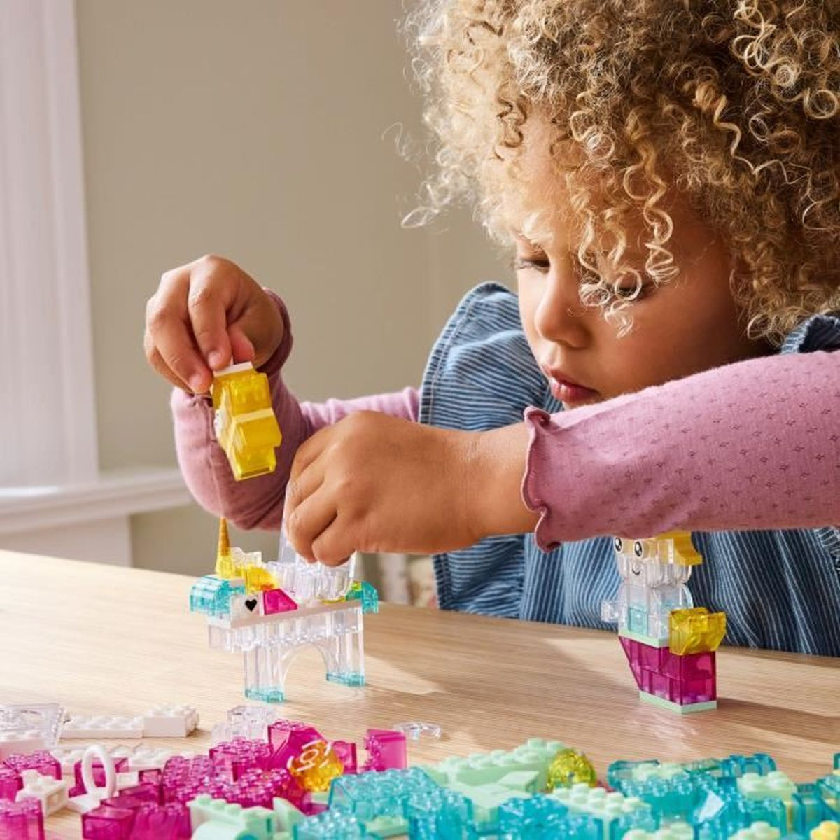 Dziewczynka bawiąca się Lego. Buduje jednorożca z przezroczystych klocków.