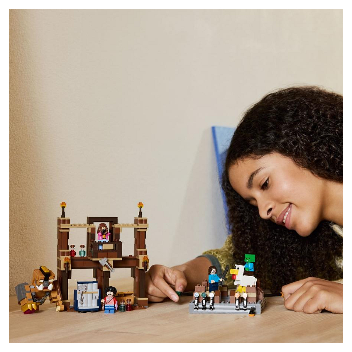 Dziewczyna obserwująca scenę Lego Minecraft z figurkami i strukturami na drewnianym stole.
