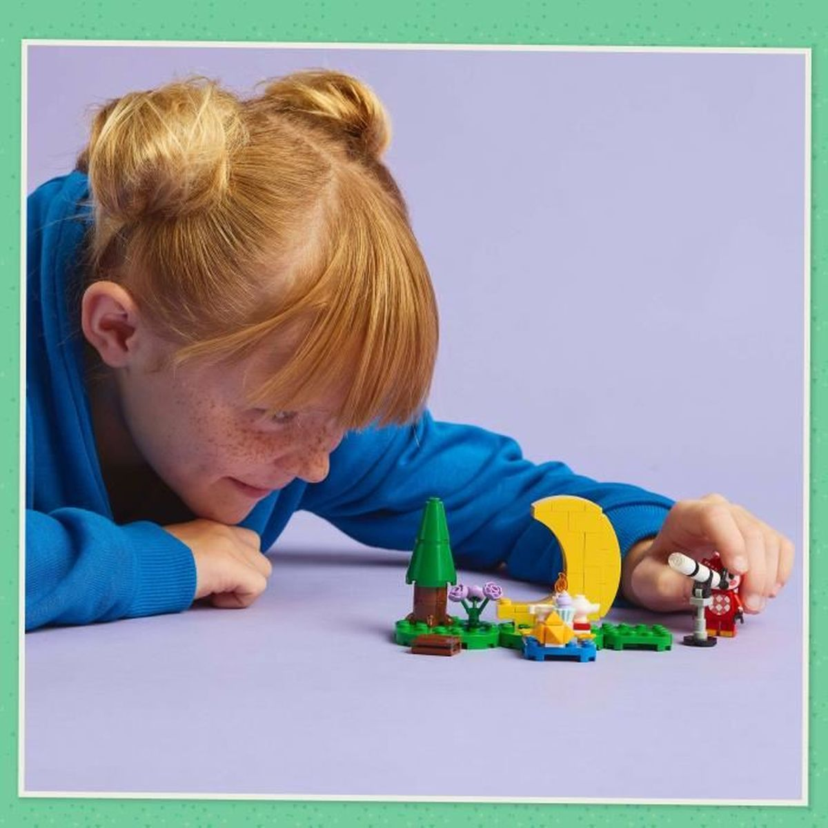 Dziecko buduje zestaw LEGO z żółtym księżycem, zielonymi drzewami i małą czerwoną konstrukcją.
