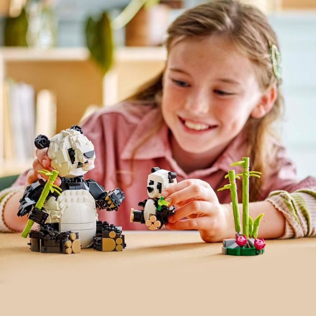 Dziewczyna bawi się pandami Lego. Jeden panda jest większy od drugiego.