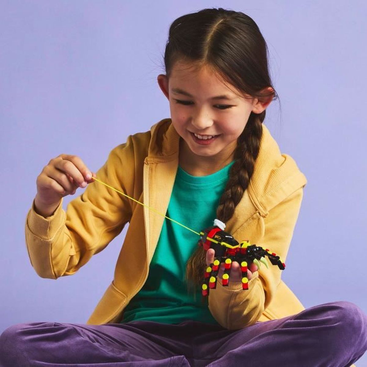 Dziewczyna z warkoczem bawi się zestawem Lego, trzymając sznurek połączony z figurką Lego przypominającą owada.