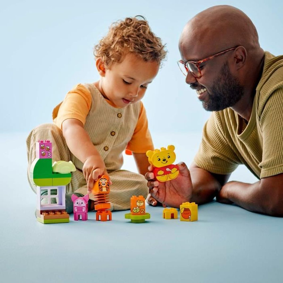 Ojciec i dziecko bawią się figurkami Lego Kubusia Puchatka i klockami.