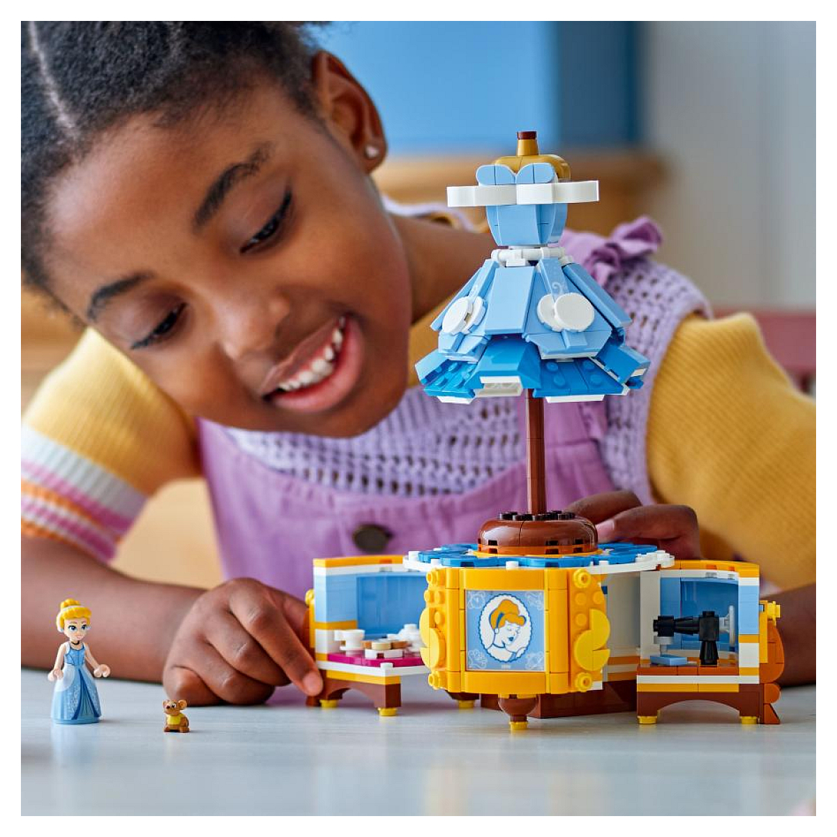 Dziewczynka bawi się niebieską karuzelą w kształcie sukienki, z figurką Kopciuszka i małymi figurkami misiów.