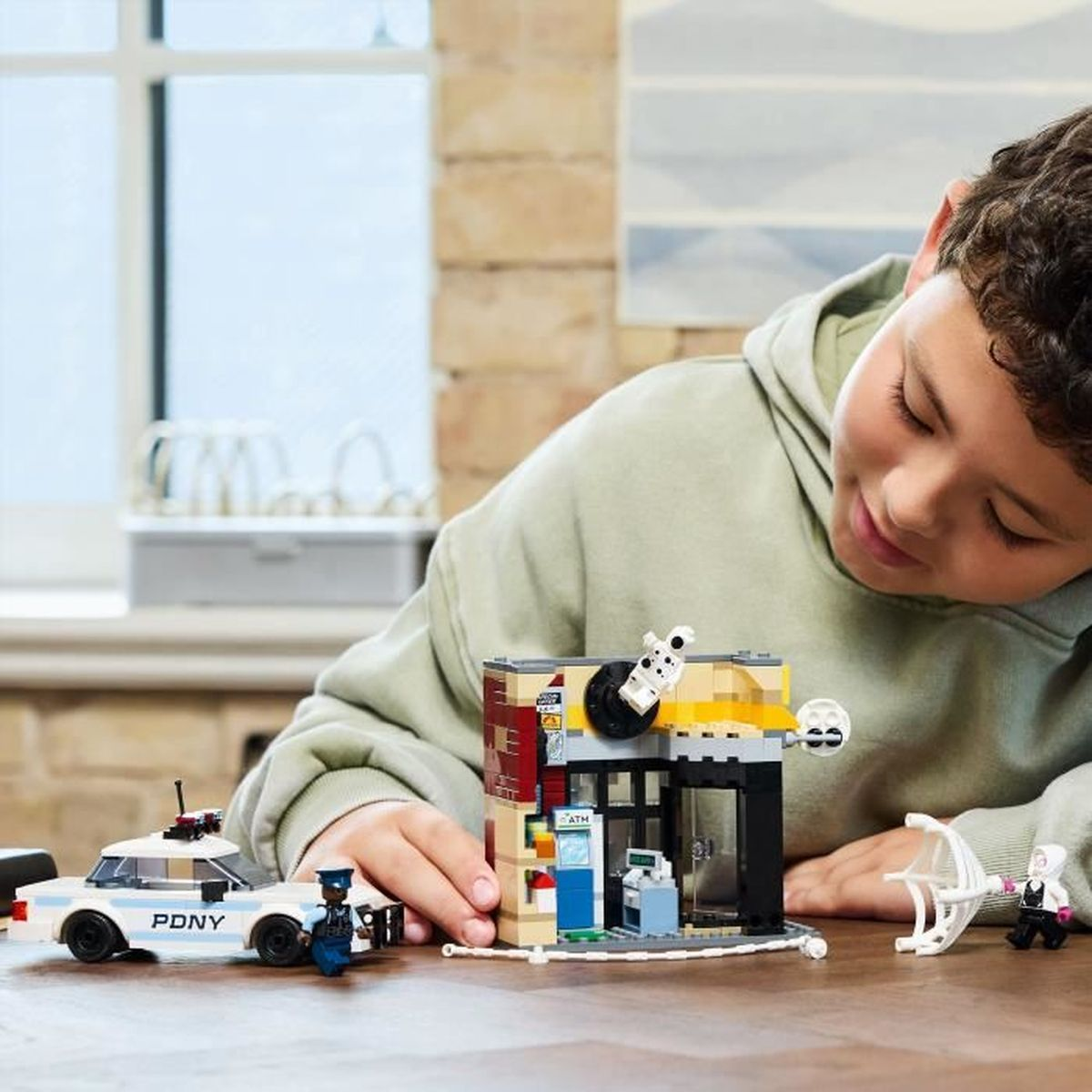 Un niño está jugando con un set de Lego que presenta un coche de policía y un edificio con un banco.