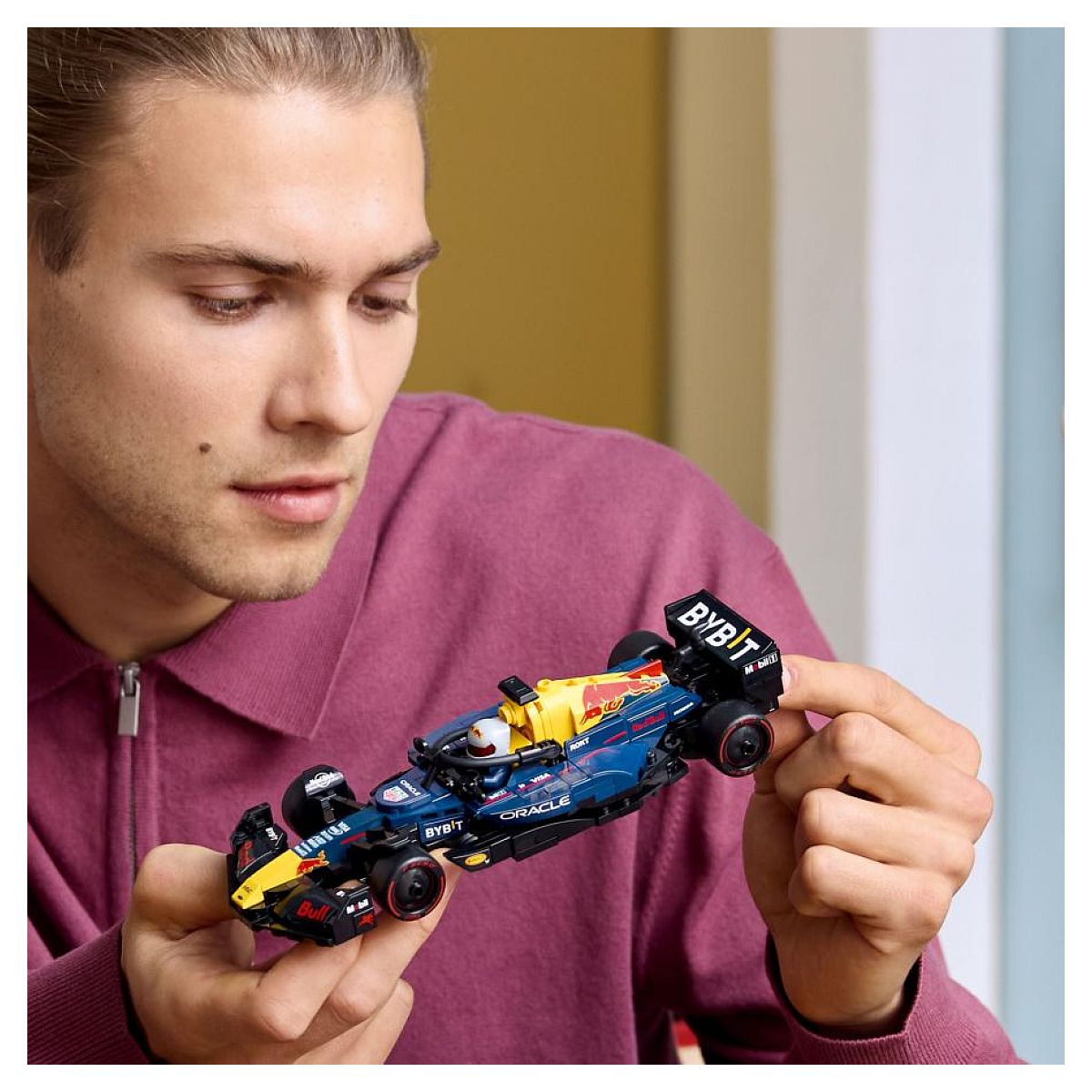 Osoba trzyma samochód Formuły 1 Lego, który jest niebiesko-żółty. Osoba na niego patrzy.