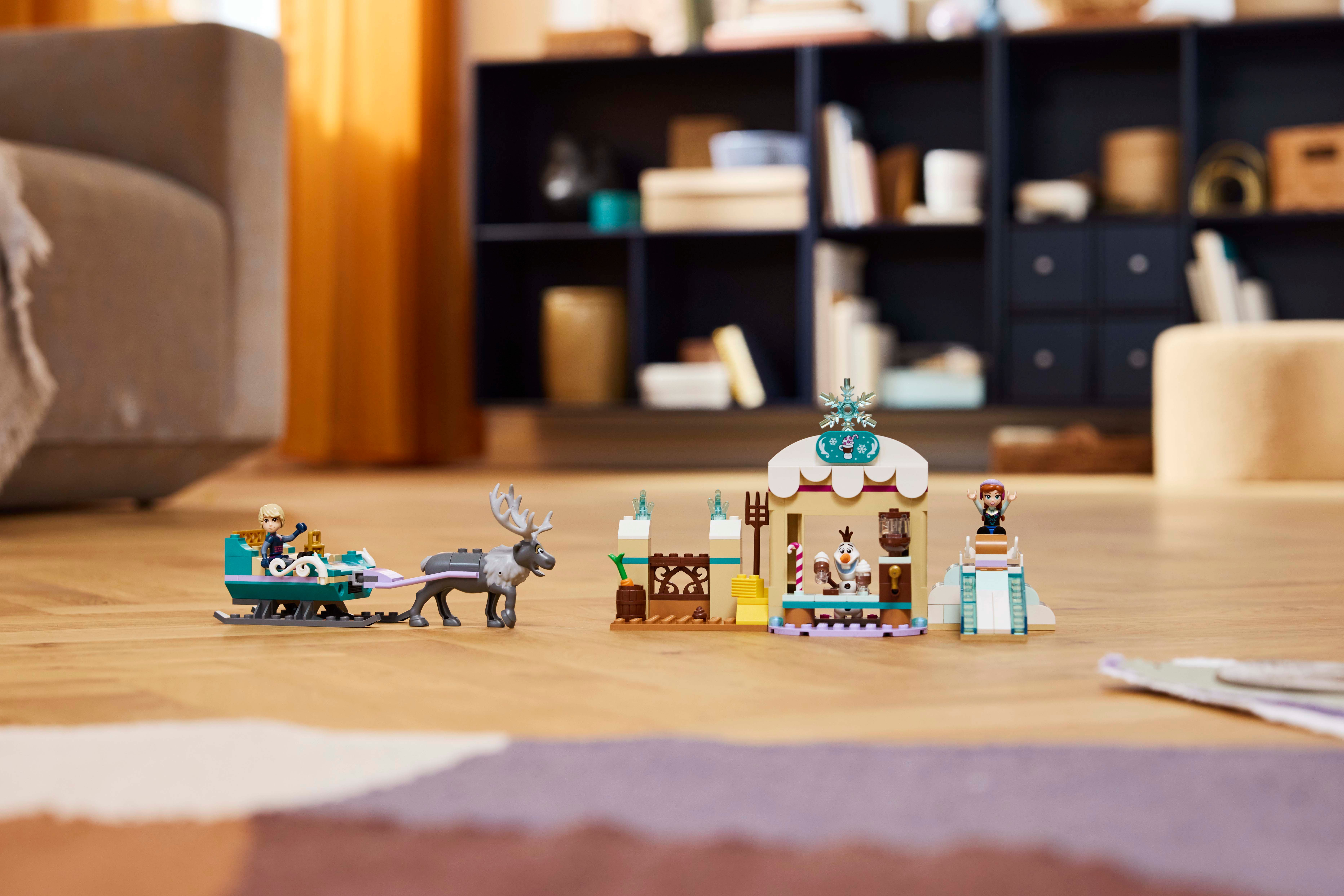 Una escena LEGO de Frozen con Anna, Elsa, Sven y un edificio se muestra en un piso de madera.