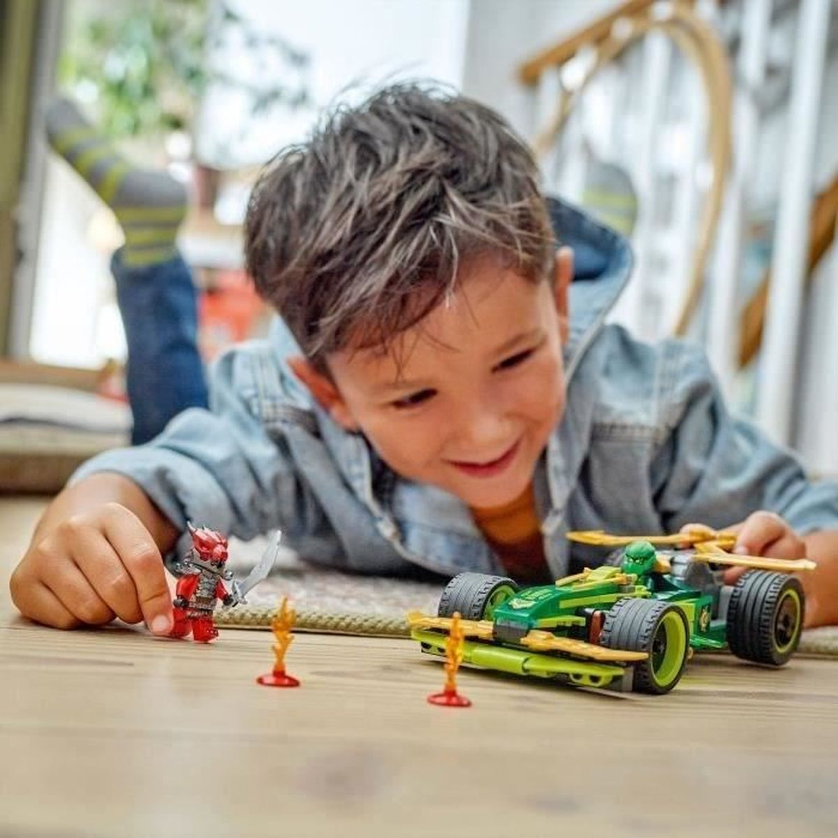 Mały chłopiec bawi się zestawem Lego Ninjago, z samochodem wyścigowym i minifigurkami na drewnianej podłodze.