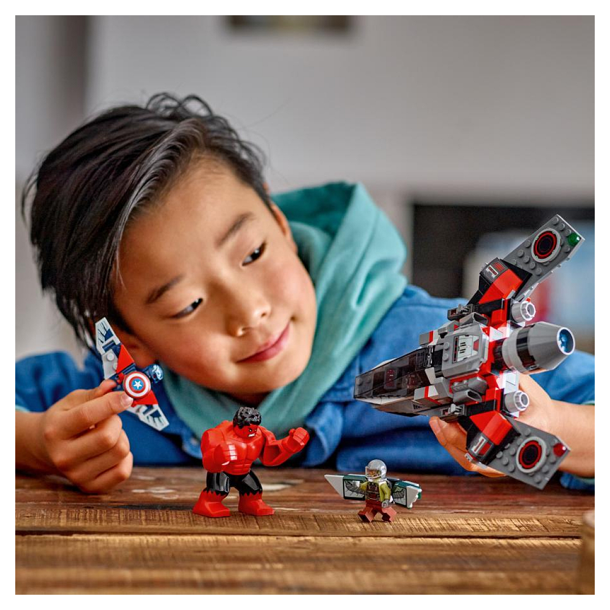 Ein Kind spielt mit Lego Marvel Figuren und einem Flugzeug, mit einem Holztisch im Vordergrund.
