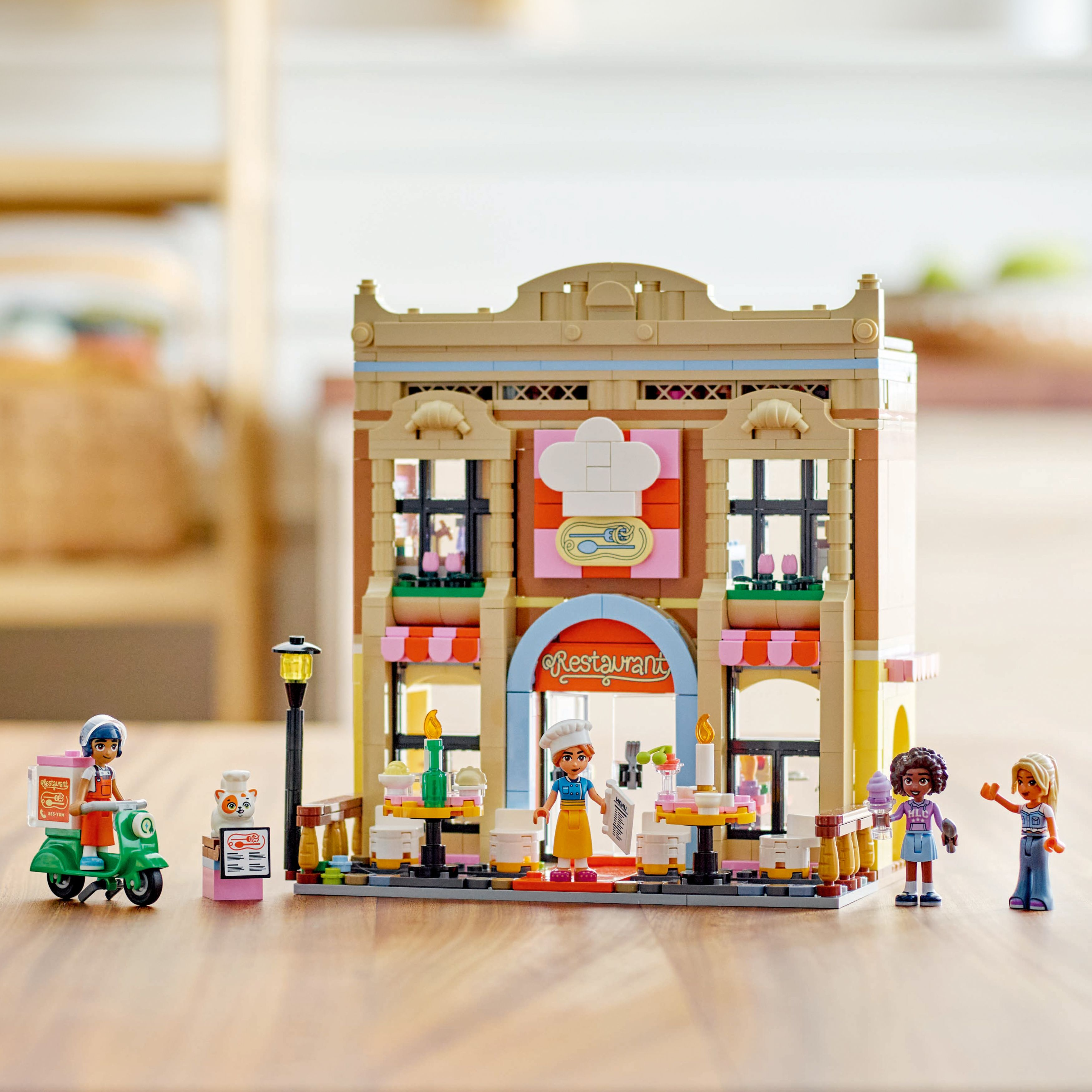 Zestaw restauracji LEGO Friends. Budynek z figurkami, skuterem i stołami. Różowe i beżowe kolory.