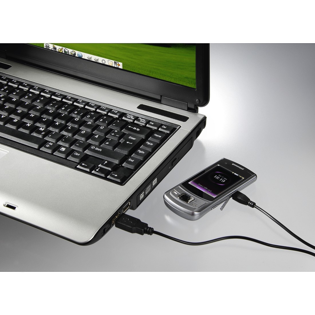 Una computadora portátil está conectada a un teléfono con un cable negro. El teléfono muestra la hora.