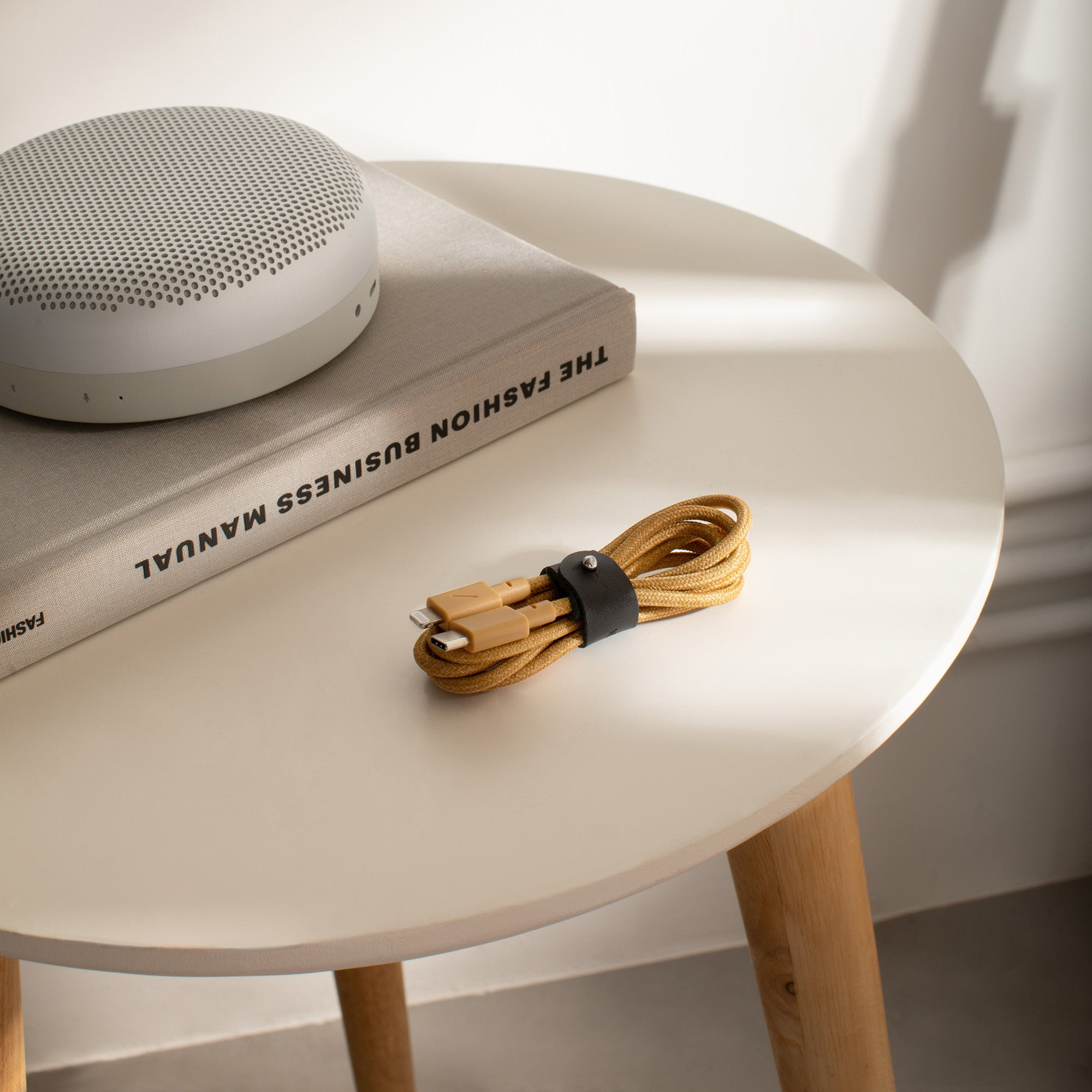 Ein runder beiger Lautsprecher und ein Buch auf einem weißen Tisch, mit gelbem Kabel.