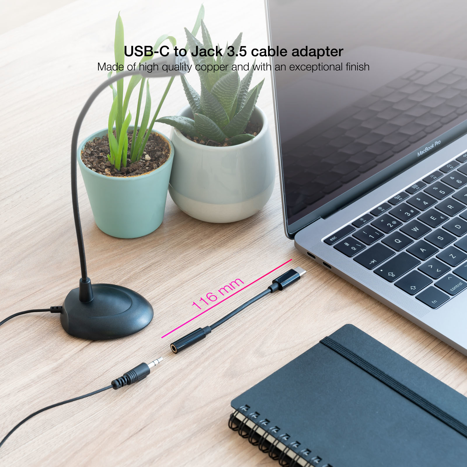 Un adattatore per cavo da USB-C a Jack 3,5 mm, nero, collegato a un laptop, con piante e un taccuino.