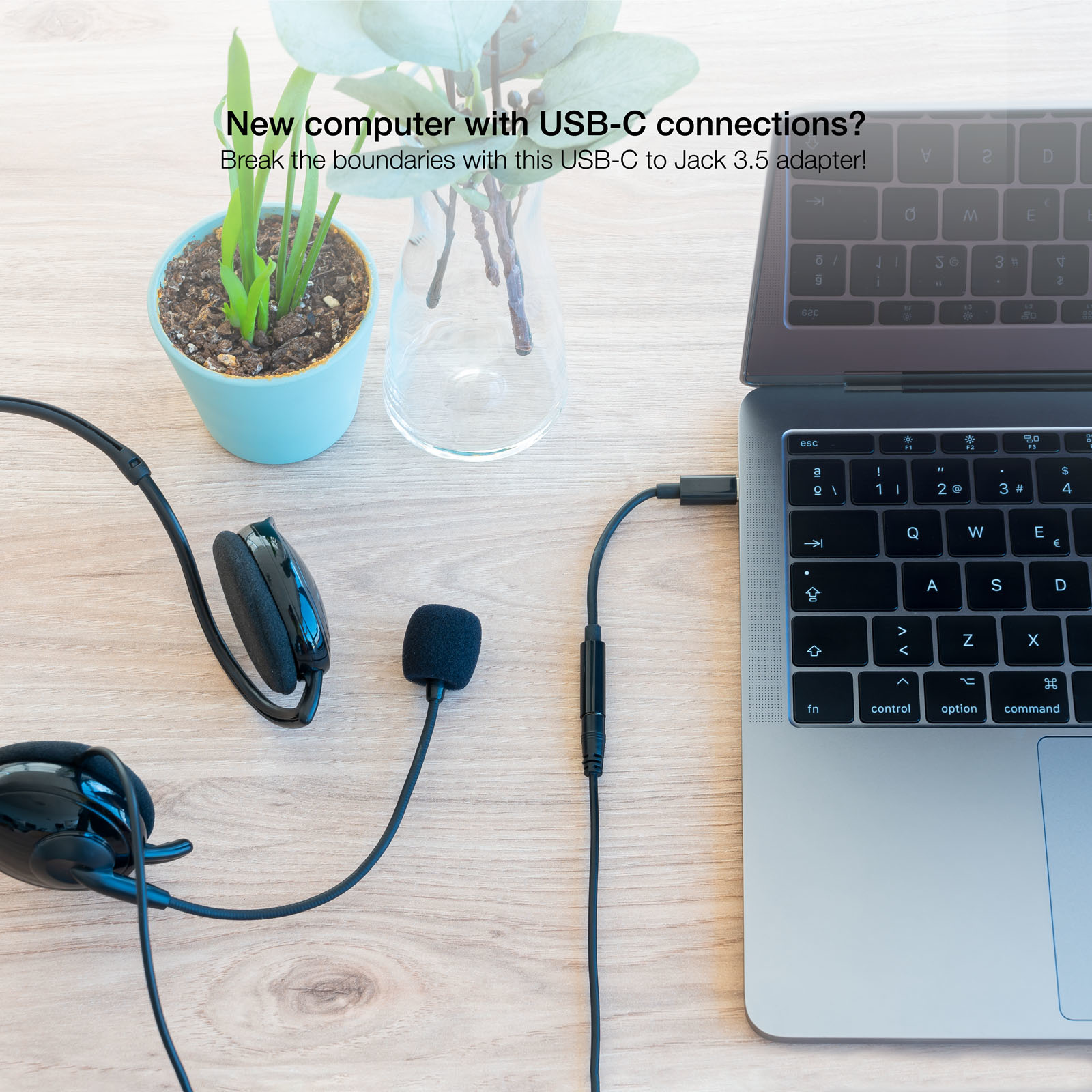 Laptop con adattatore USB-C a 3.5mm e cuffie, su tavolo di legno con pianta.