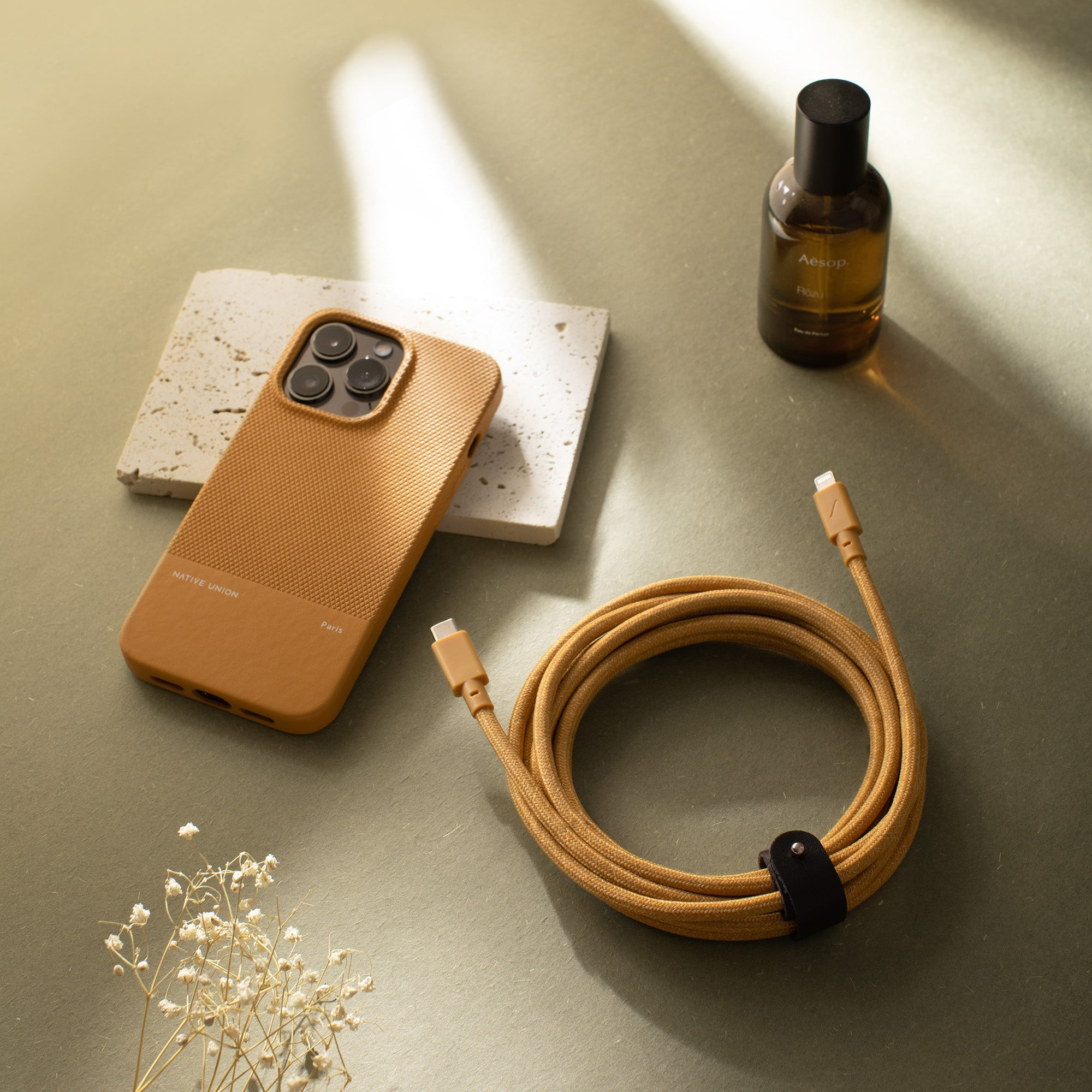 Una custodia per telefono, una bottiglia di profumo e un cavo con connettore USB-C, disposti su una superficie.