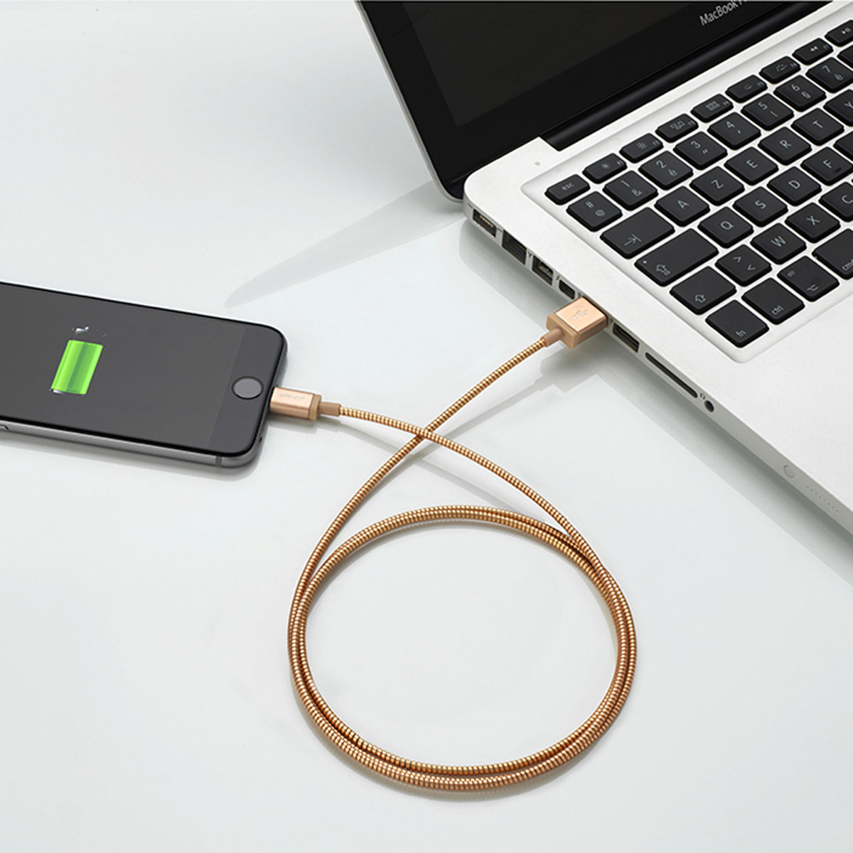 Un téléphone en charge à côté d'un ordinateur portable. Un câble de charge doré est connecté aux deux appareils.