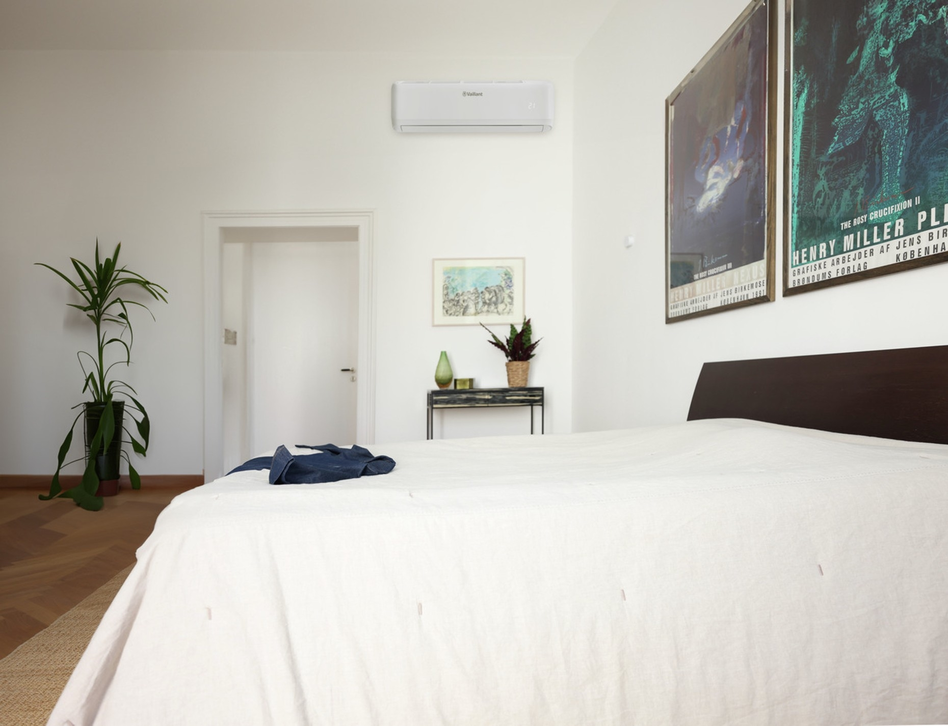 Camera da letto con letto, condizionatore e pianta. Poster appesi al muro. Una porta è aperta.
