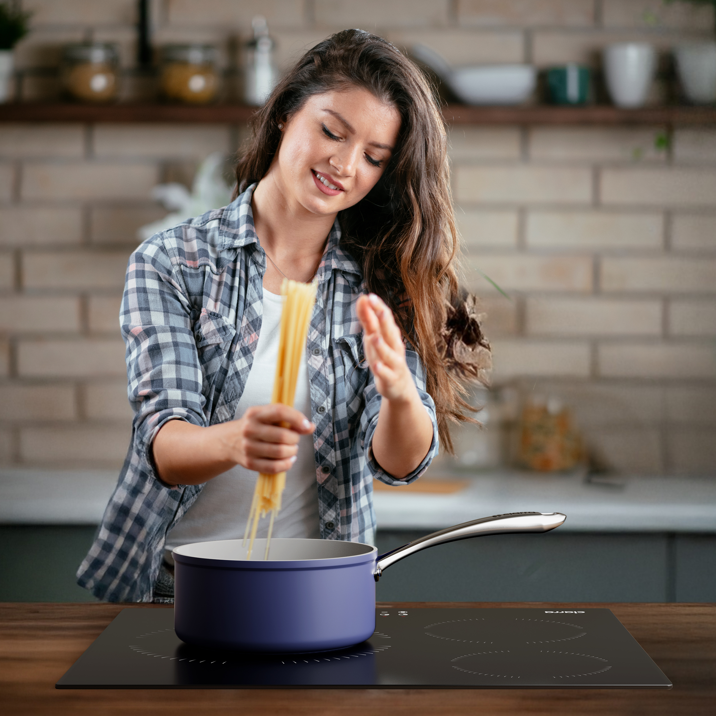 Une femme en chemise à carreaux ajoute des spaghettis à une casserole bleue sur une plaque de cuisson noire.