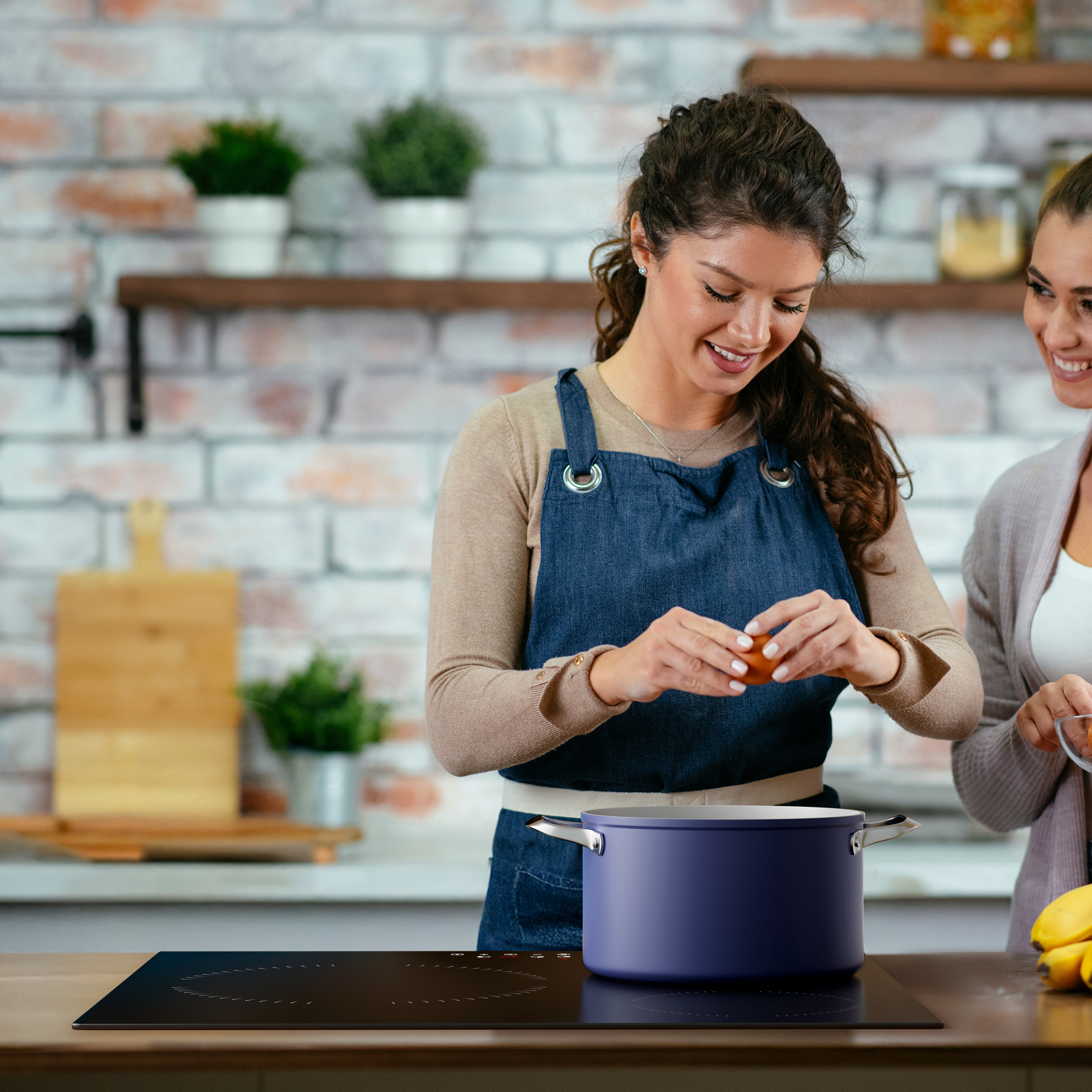 Deux femmes dans une cuisine, l'une cassant un œuf dans une casserole sur une cuisinière.