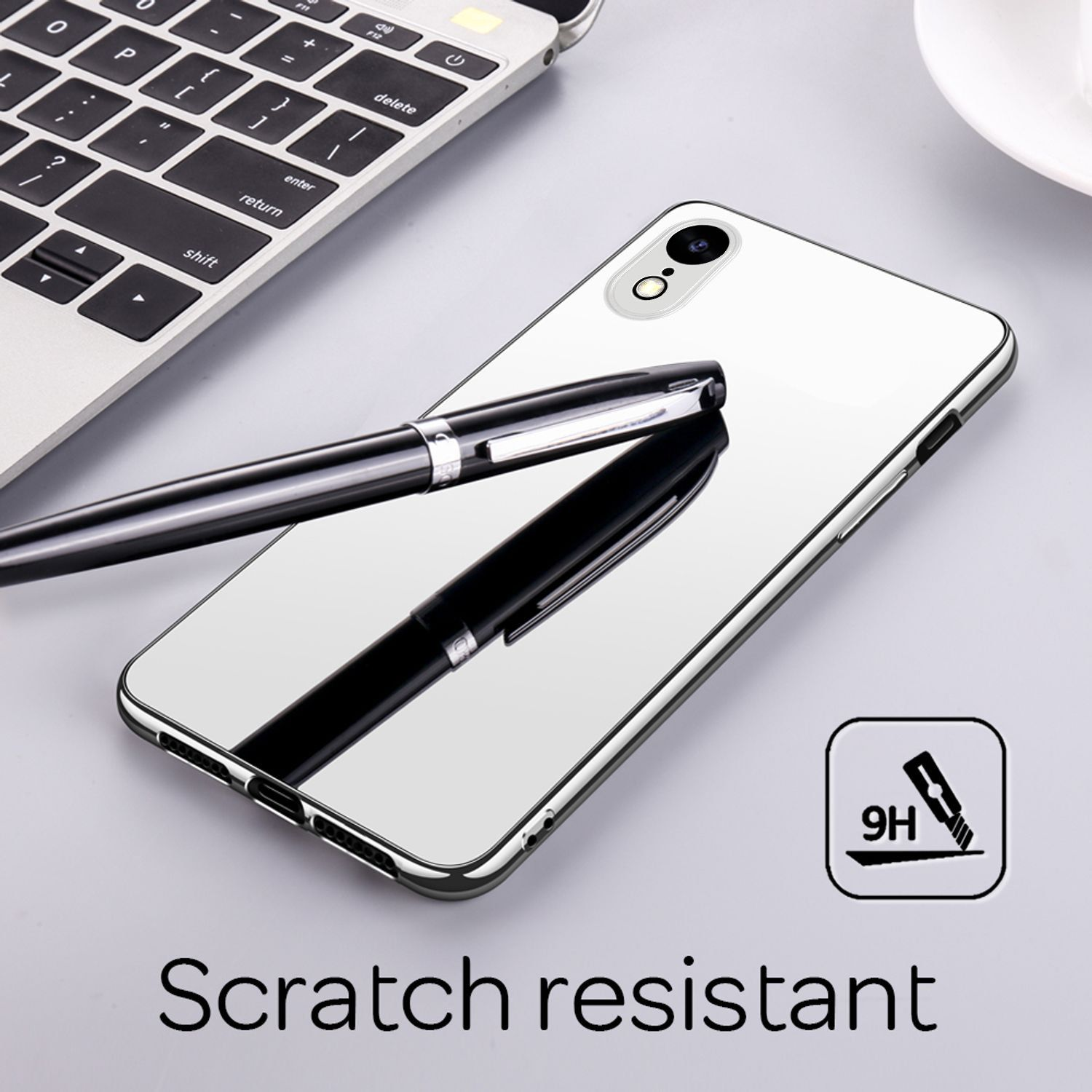 Ein Telefon mit spiegelähnlicher Rückseite, ein Stift und ein Laptop liegen auf grauer Oberfläche.